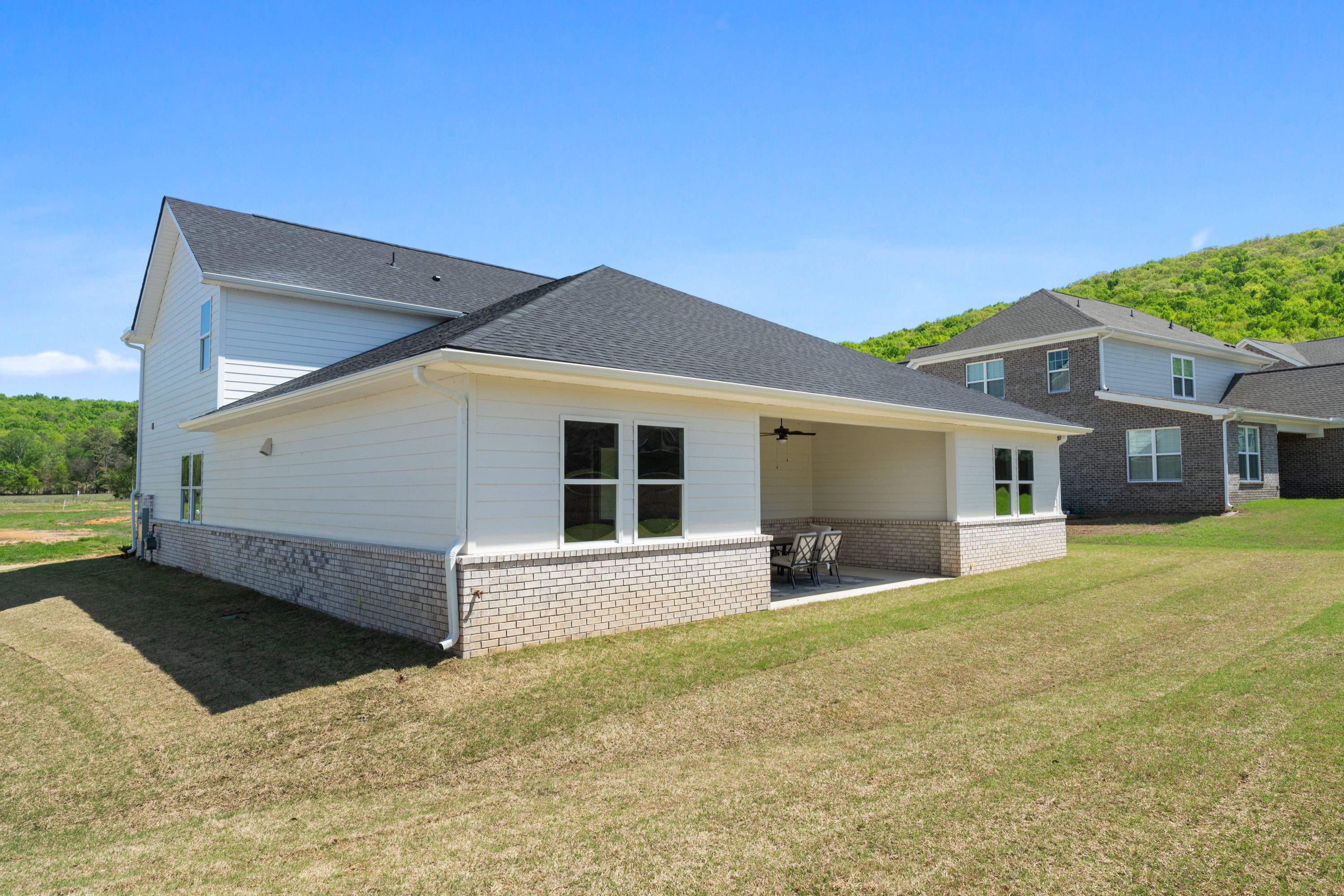 Rear view of The Haven single-story home with covered patio, brick accents, and lush lawn in Owens Cross Roads