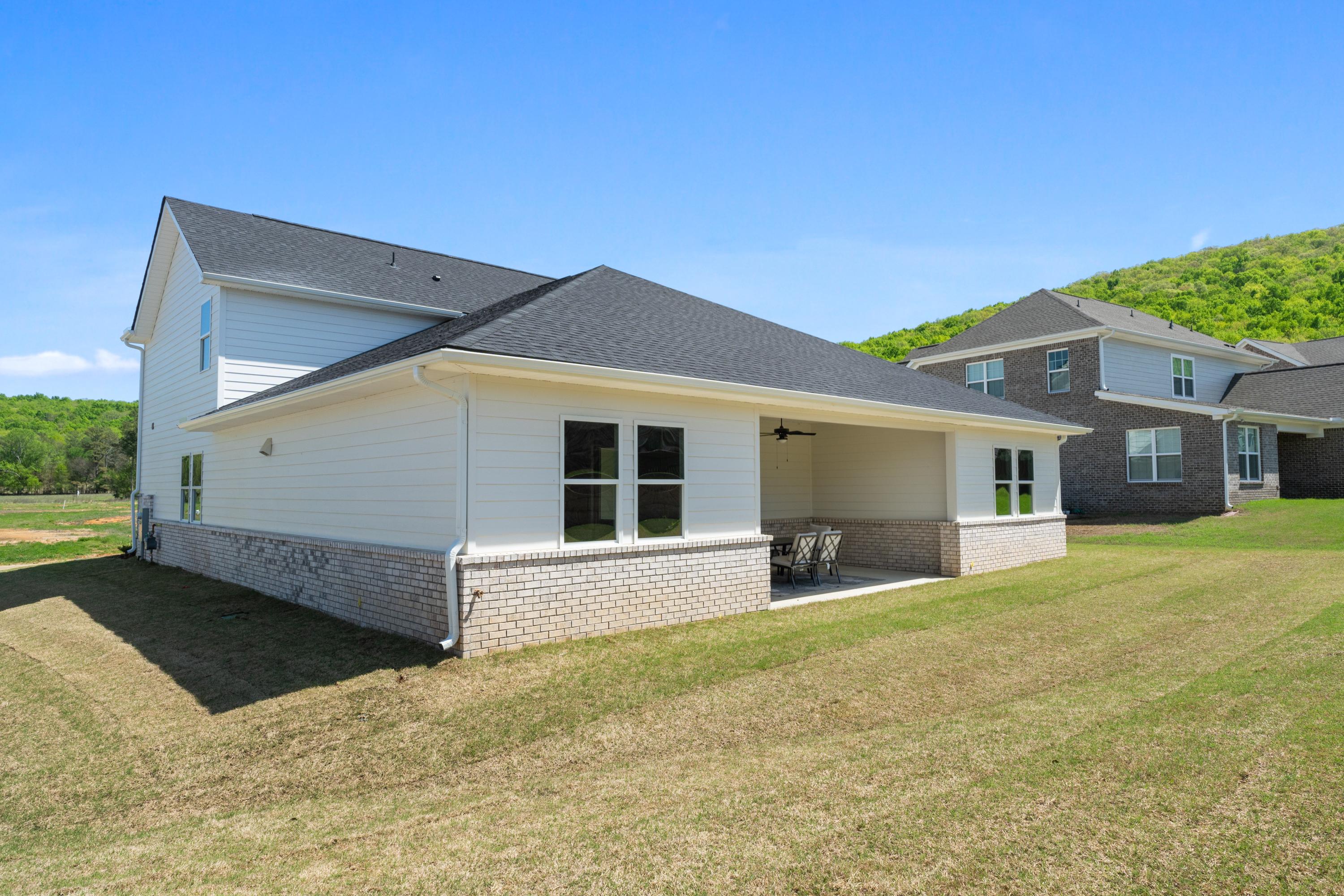 Rear view of The Haven single-story home with covered patio, brick accents, and lush lawn in Owens Cross Roads