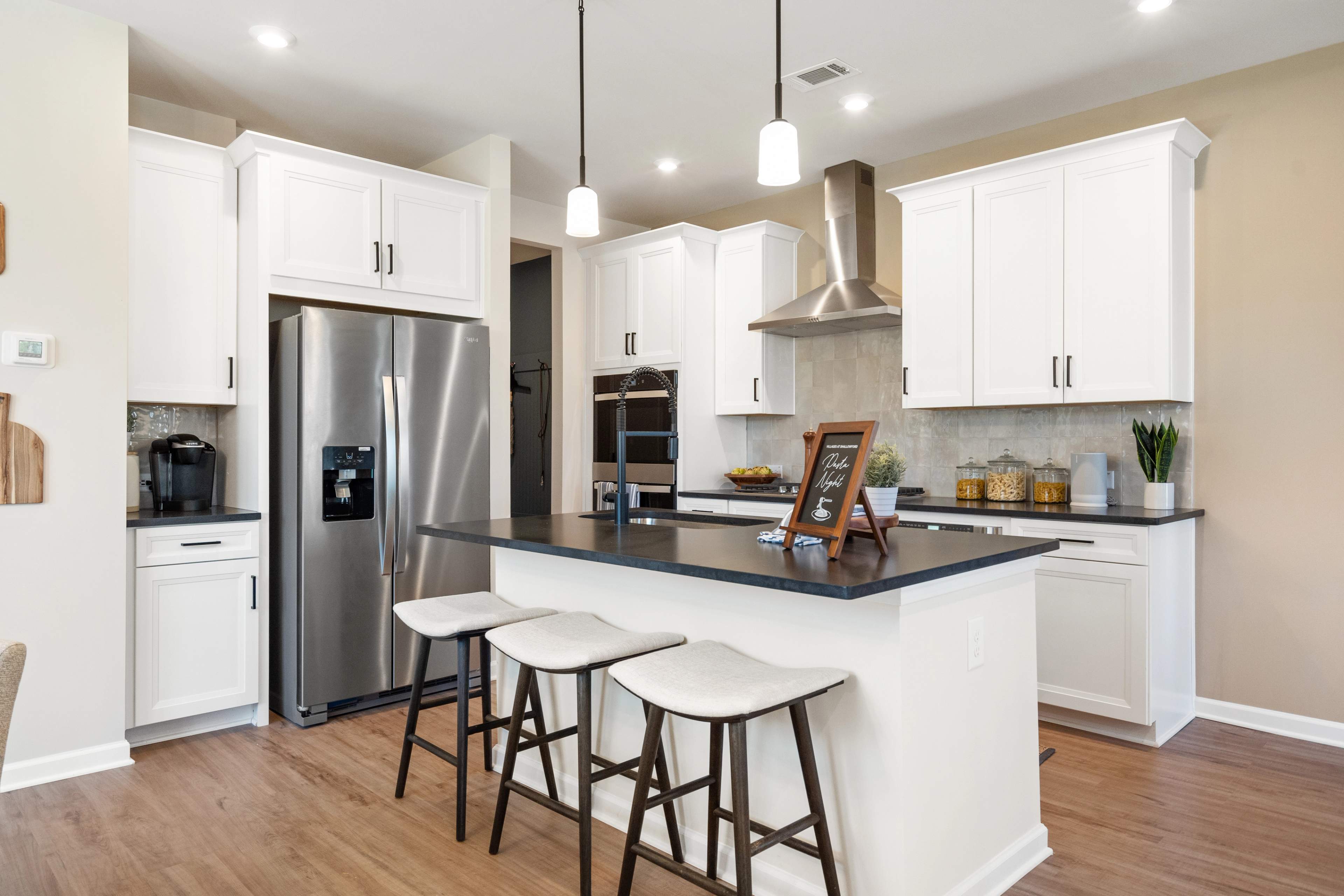 Spacious modern kitchen at The Bluffs in Canton GA by Davidson Homes with white cabinetry, stainless steel appliances, and island bar