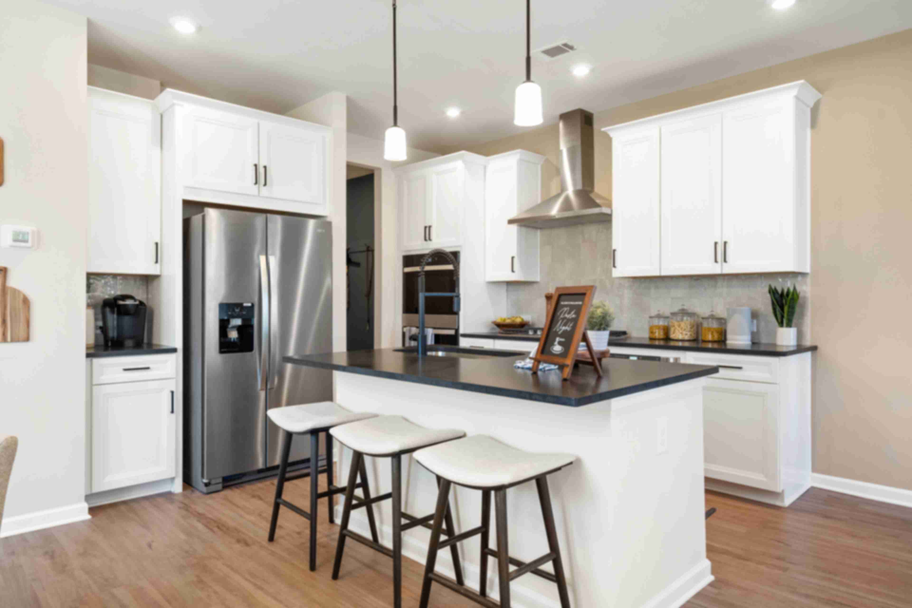 Spacious modern kitchen at The Bluffs in Canton GA by Davidson Homes with white cabinetry, stainless steel appliances, and island bar