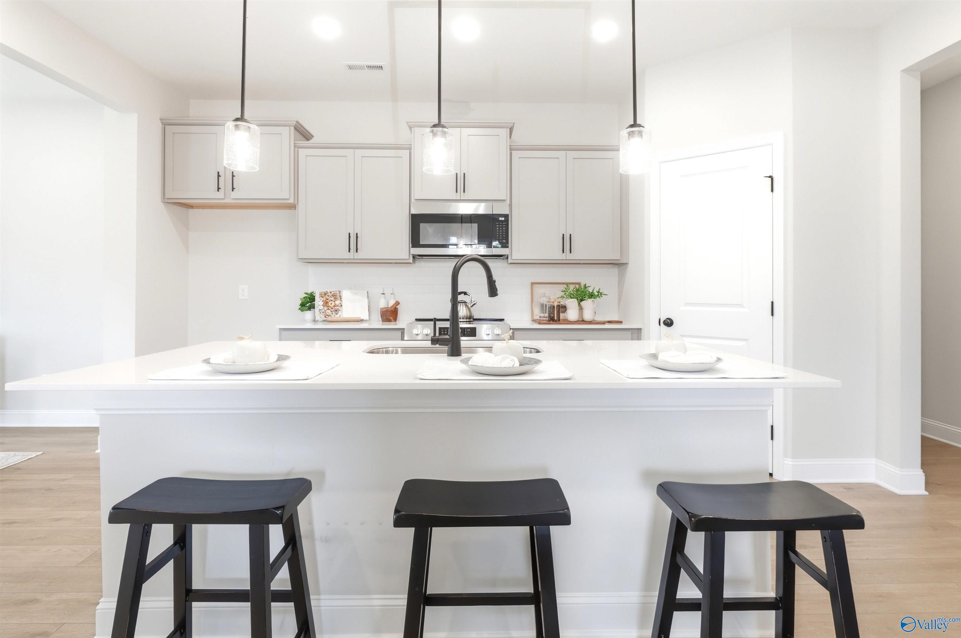 Bright kitchen island with pendant lights, white cabinetry, and black barstools in Davidson Homes The Russell A, Huntsville, AL
