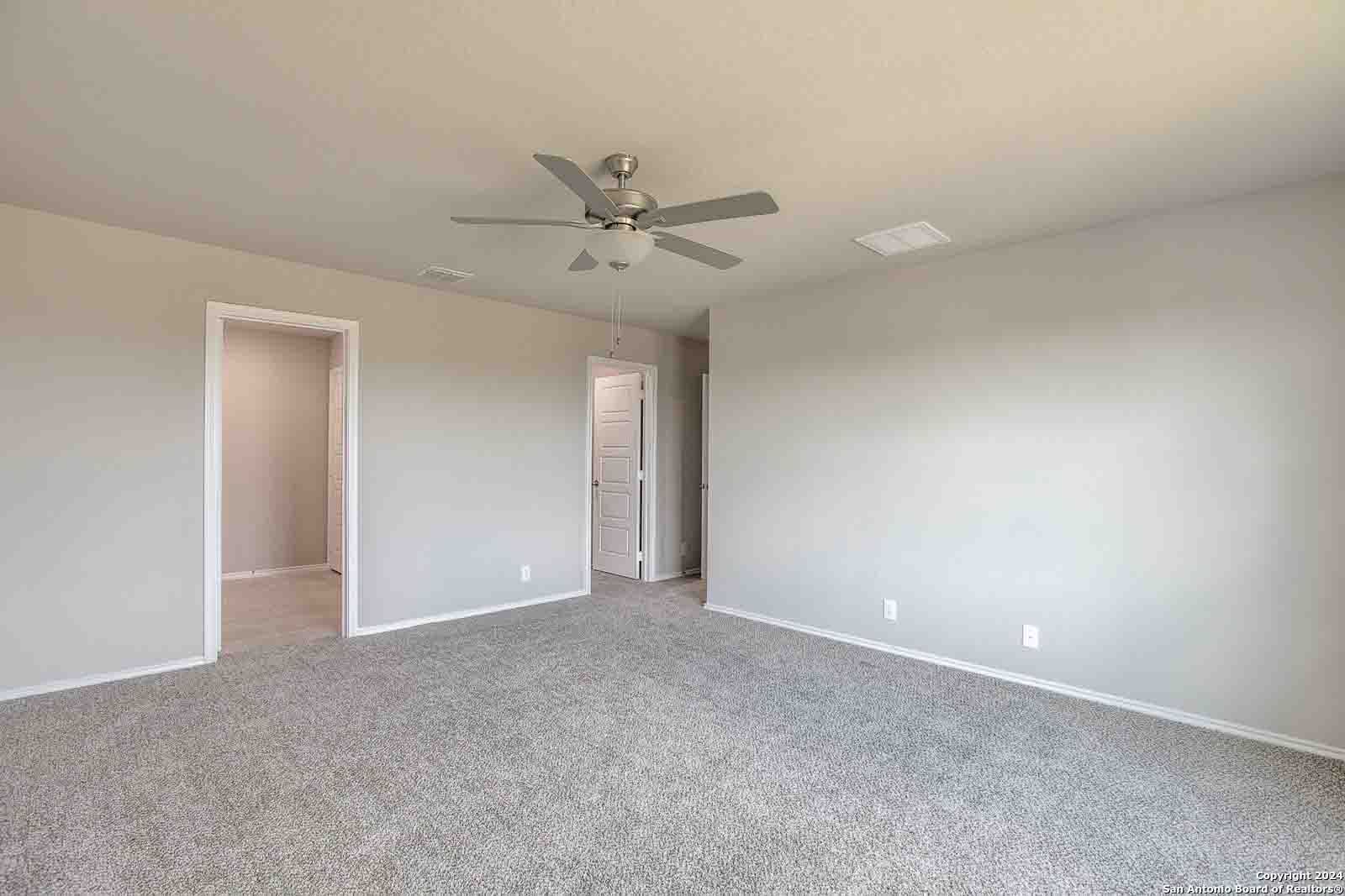 Spacious empty bedroom with ceiling fan, beige walls, gray carpet, and adjacent doorways in Davidson Homes The Murray H, Seguin, Texas