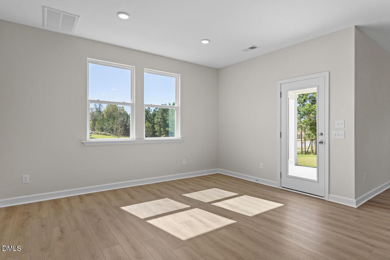 Bright empty room with luxury vinyl plank flooring, double windows, and glass-paneled door in Davidson Homes Preston B plan, Wendell NC