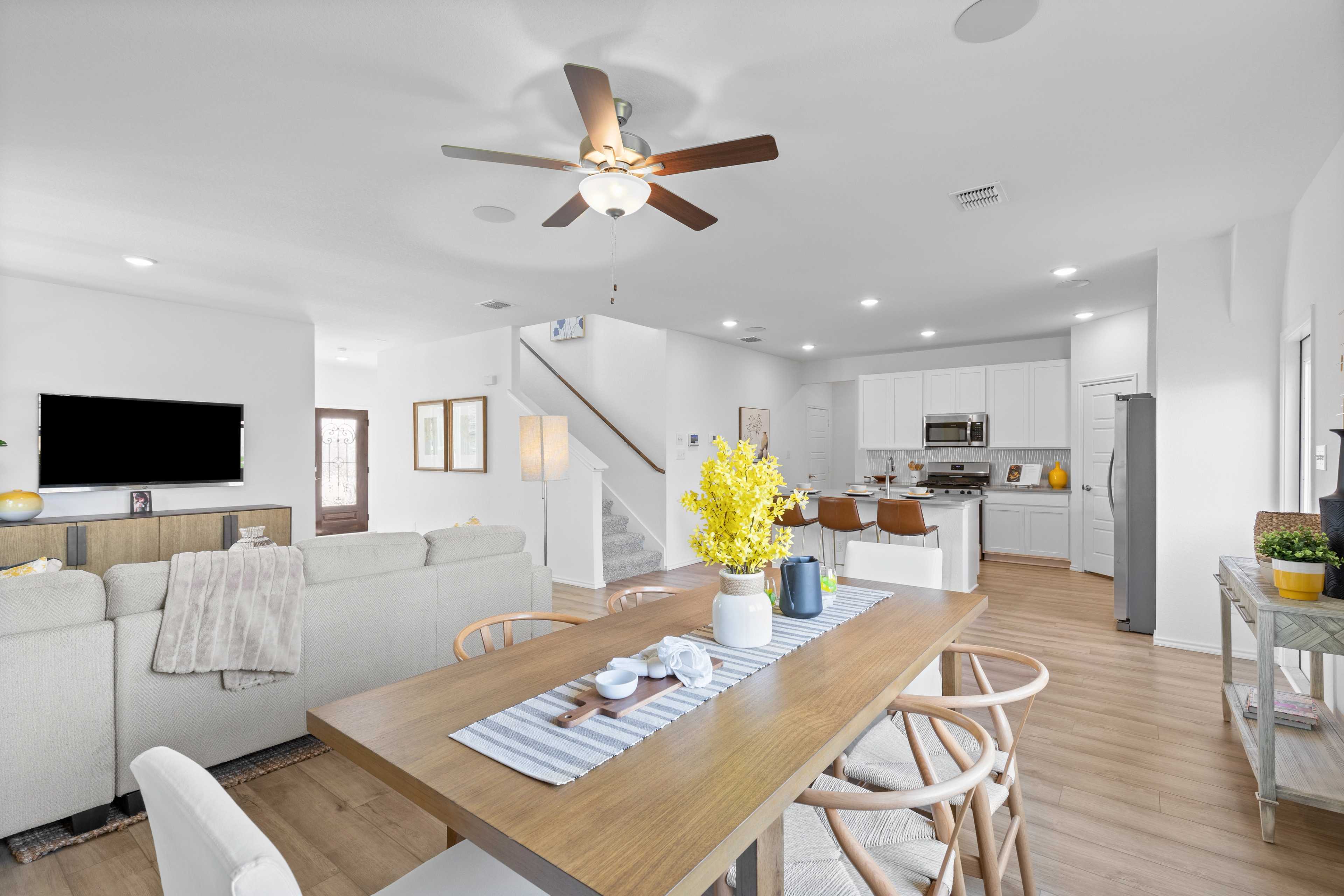 Open-concept living room and kitchen in Horizon Pointe Converse Texas home with hardwood floors, white cabinets, wooden dining table, and yellow floral accents