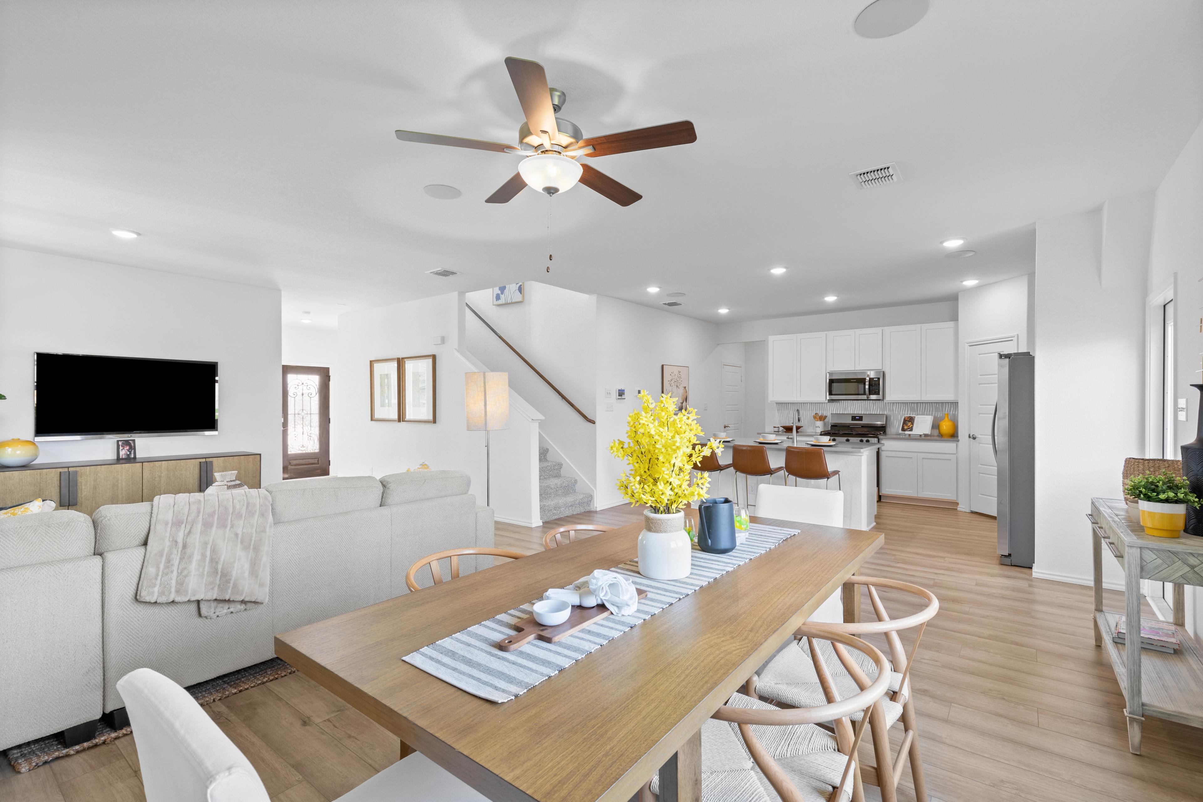 Open-concept living room and kitchen in Horizon Pointe Converse Texas home with hardwood floors, white cabinets, wooden dining table, and yellow floral accents