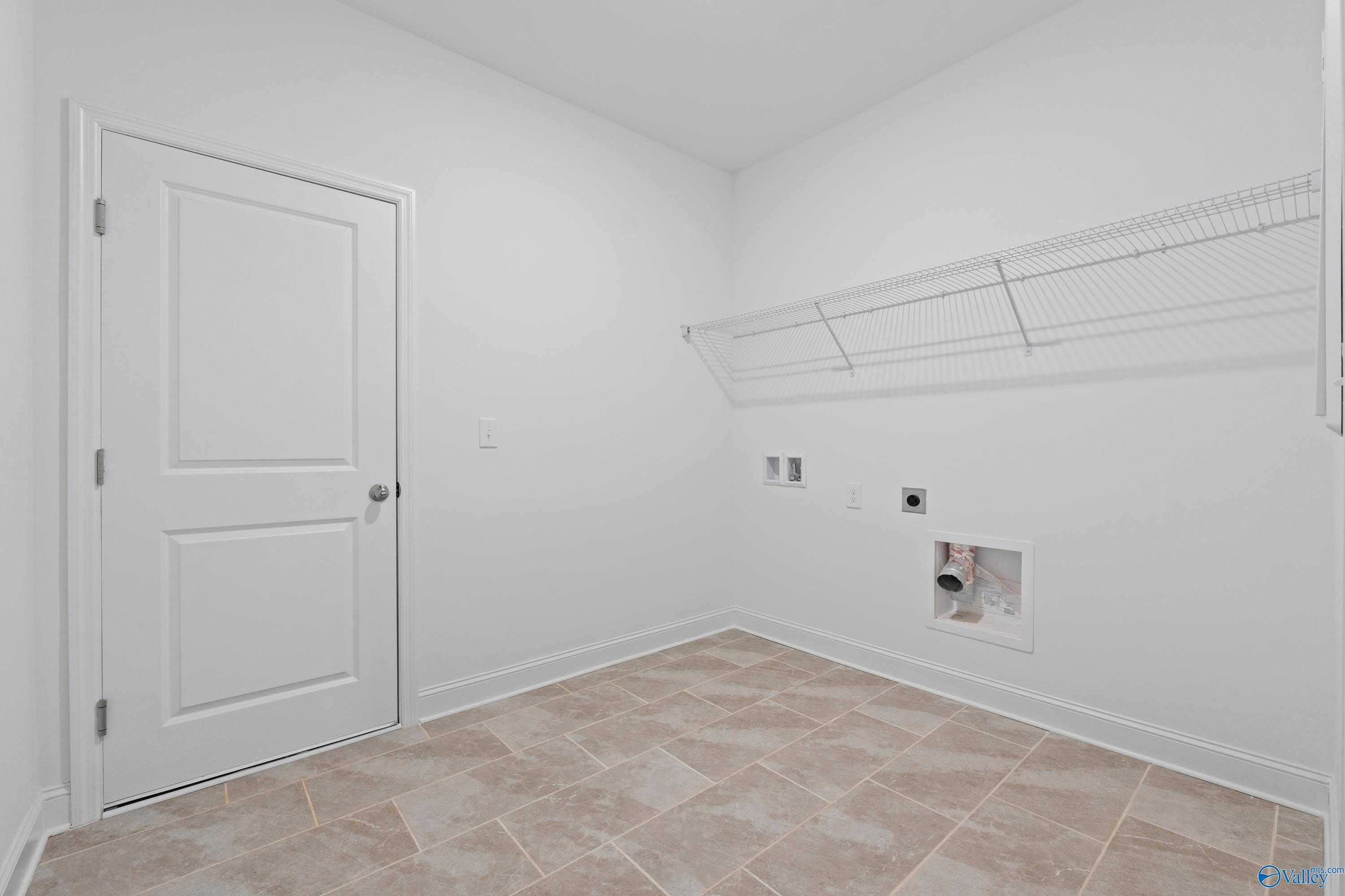 Bright laundry room with white walls, wire shelving, washer dryer hookups, beige tile floor in Davidson Homes The Oxford, Harvest AL