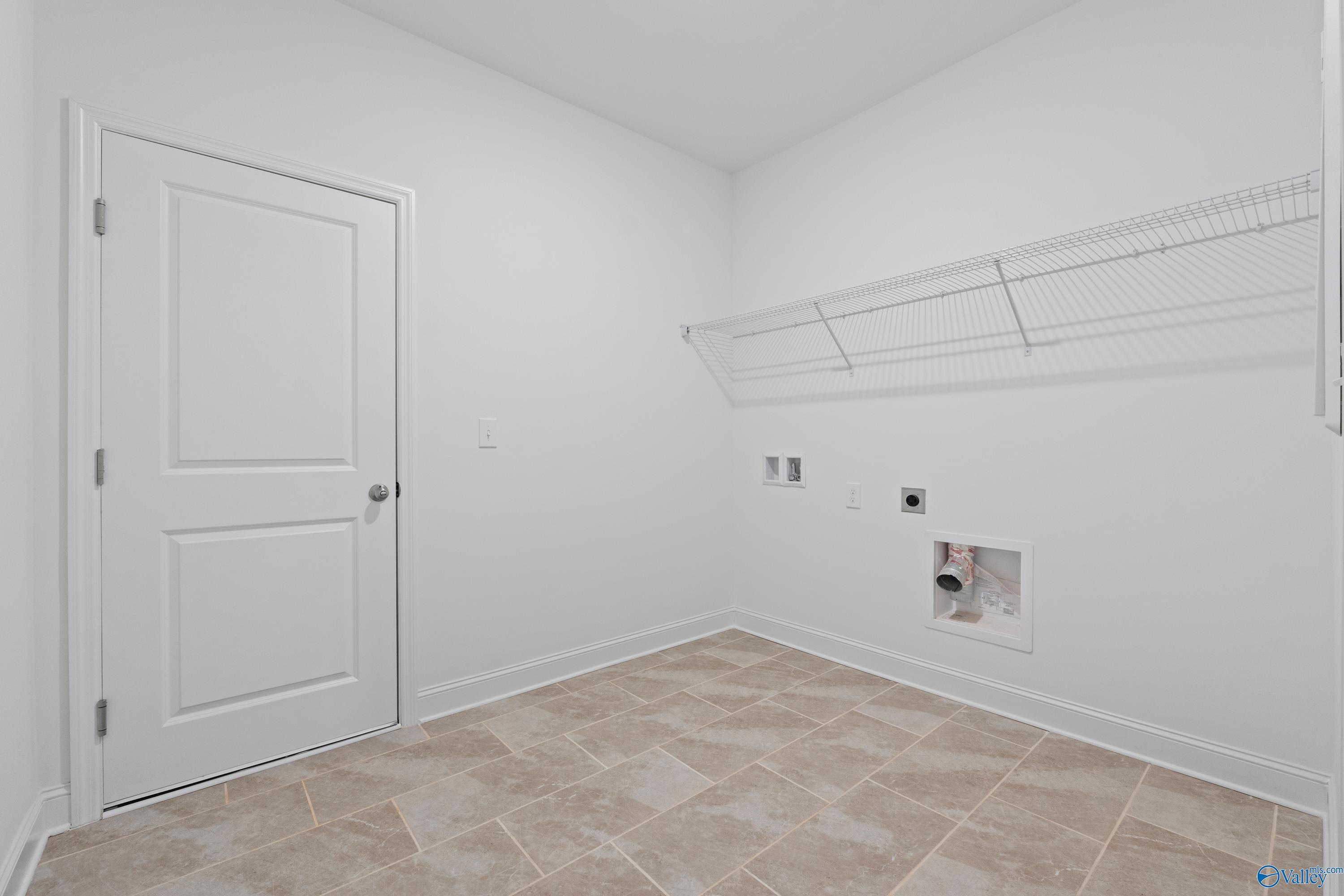 Bright laundry room with white walls, wire shelving, washer dryer hookups, beige tile floor in Davidson Homes The Oxford, Harvest AL