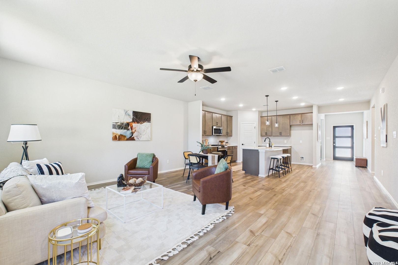 Open-concept living and kitchen area with hardwood floors, leather chairs, white island, and ceiling fan in Davidson Homes The Douglas E, San Antonio