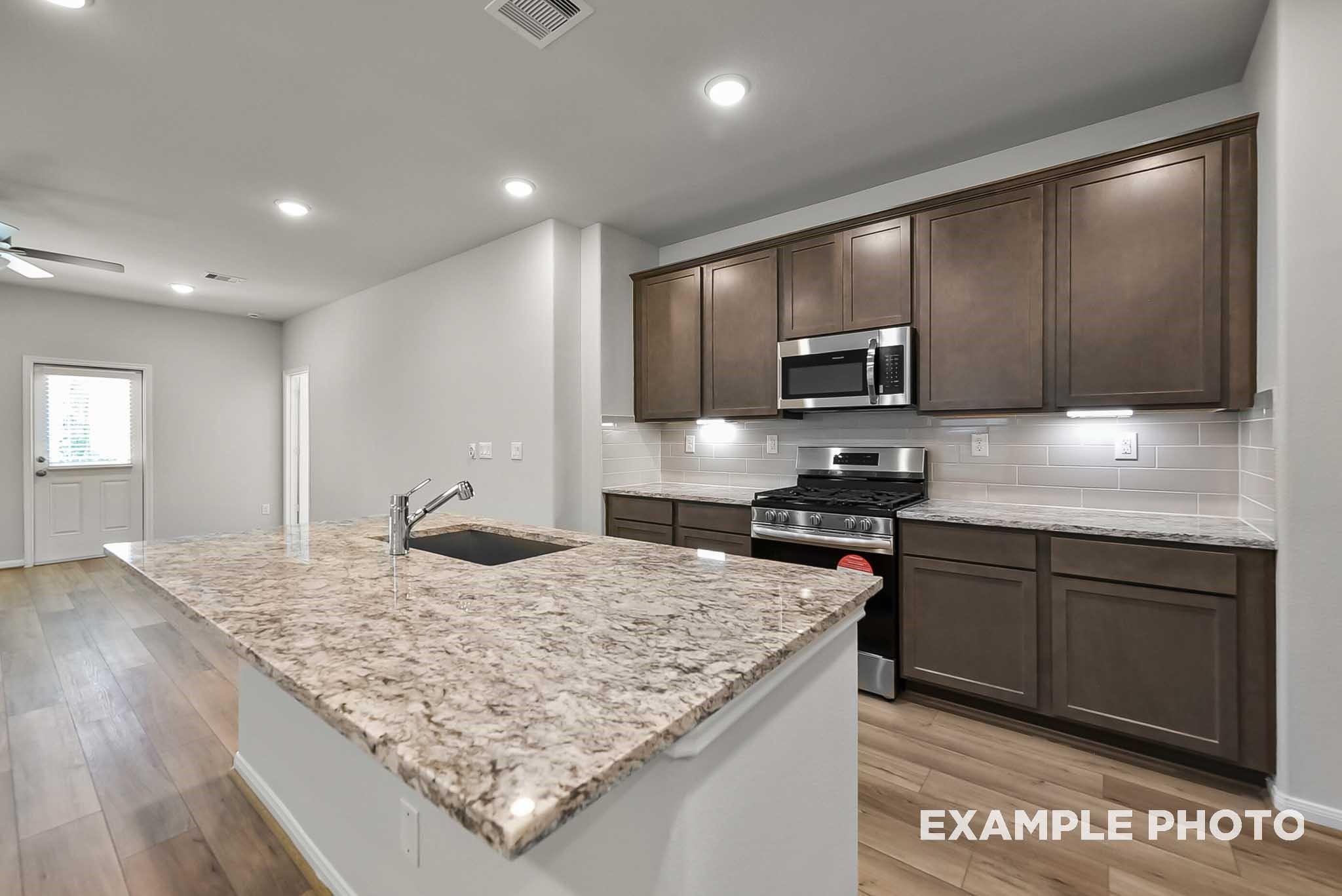 Kitchen island with granite countertops, dark wood cabinets, and stainless appliances in Davidson Homes Blanco F plan, Dayton, Texas
