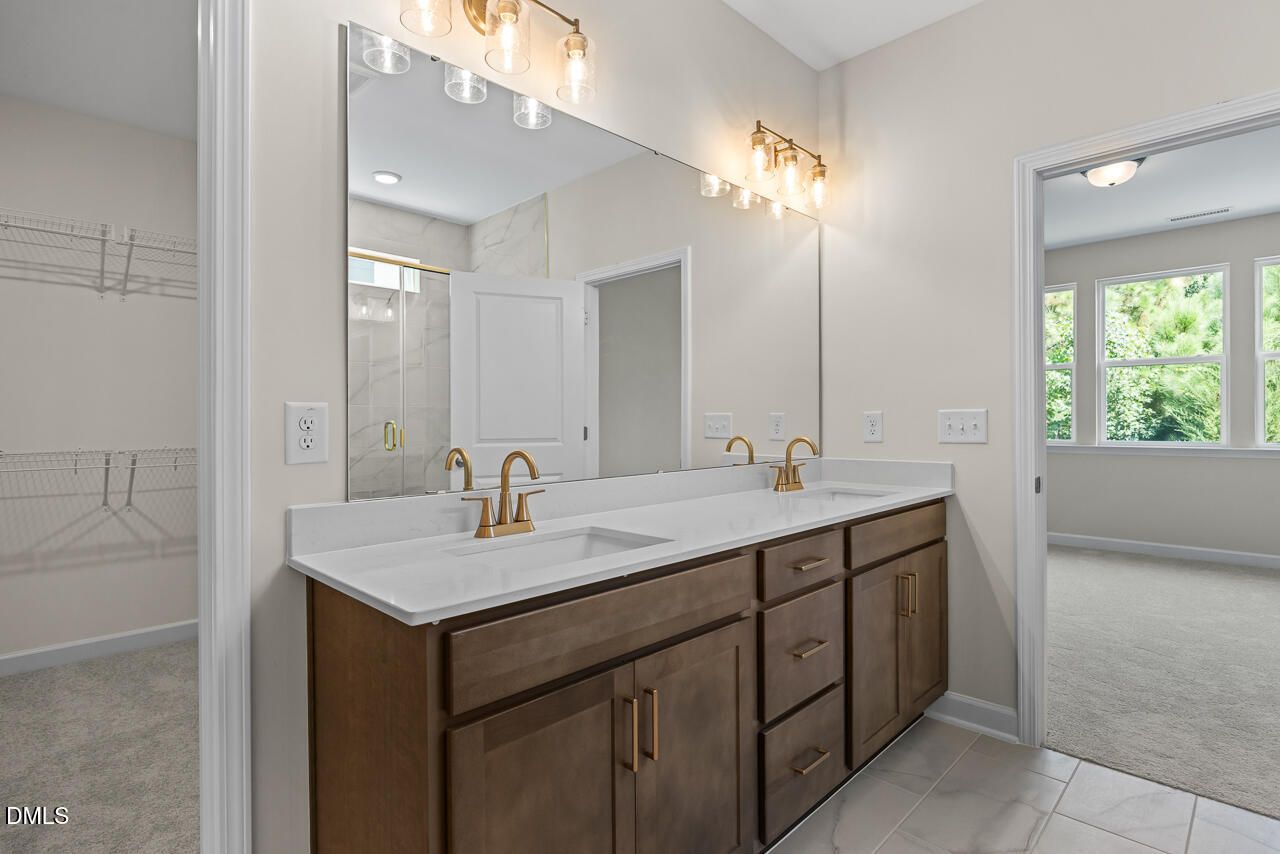 Double vanity bathroom with white countertops, gold fixtures, and large mirror in Davidson Homes The Birch II C, Wake Forest, NC
