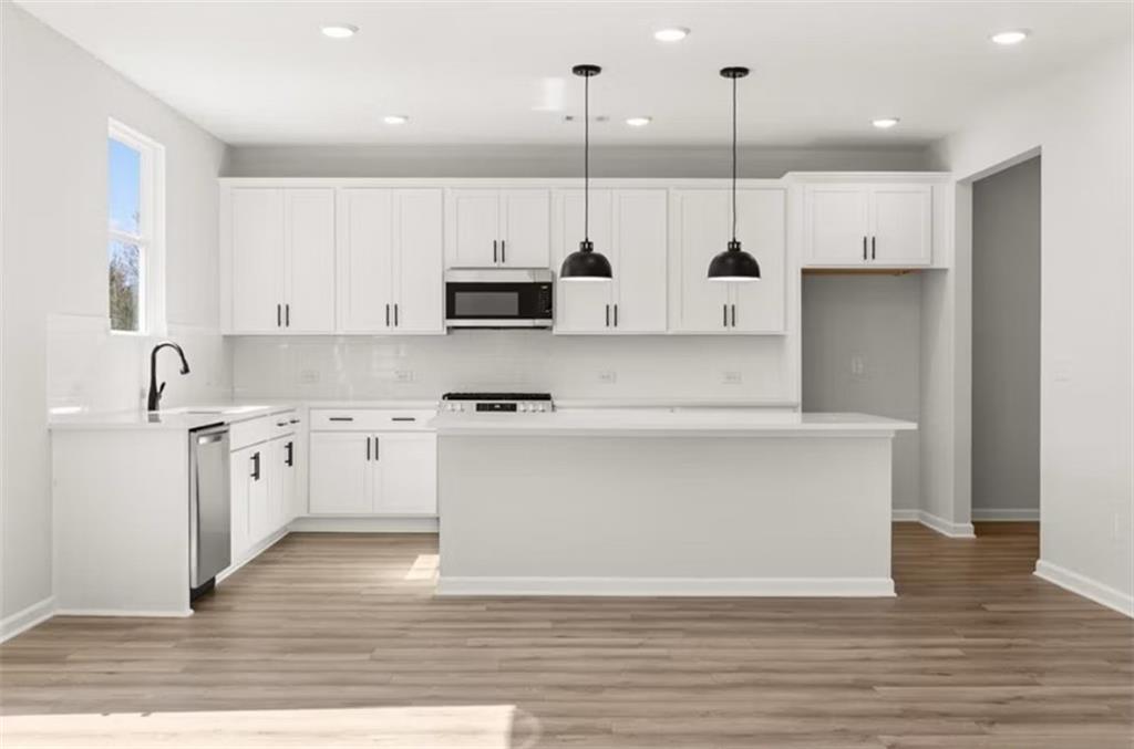 Modern white kitchen with large island, stainless appliances, black pendants in Davidson Homes Hickory B, Winder GA