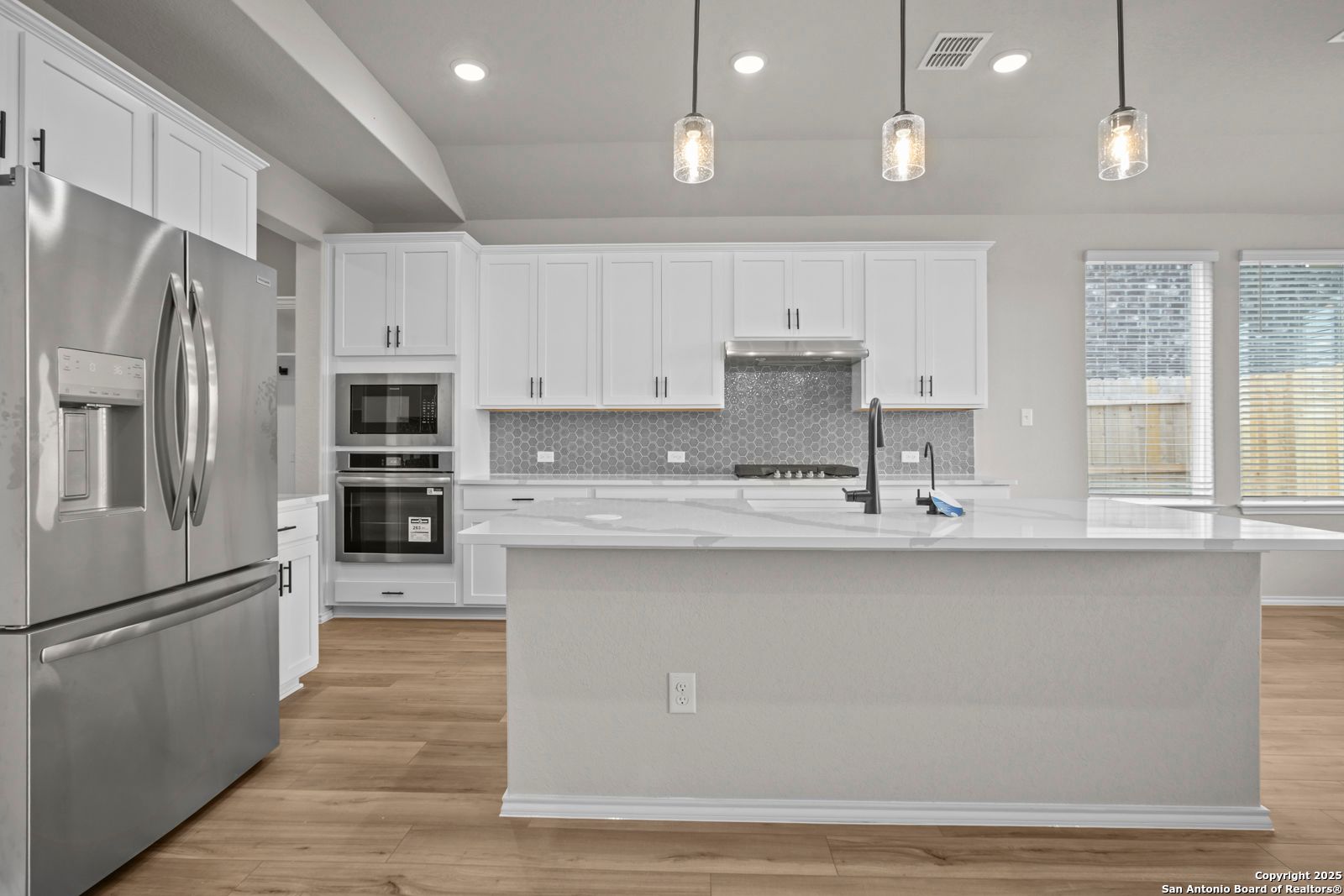Modern white kitchen with stainless steel fridge, double oven, subway tile backsplash, and large island in Davidson Homes Sequoia A, Converse, Texas