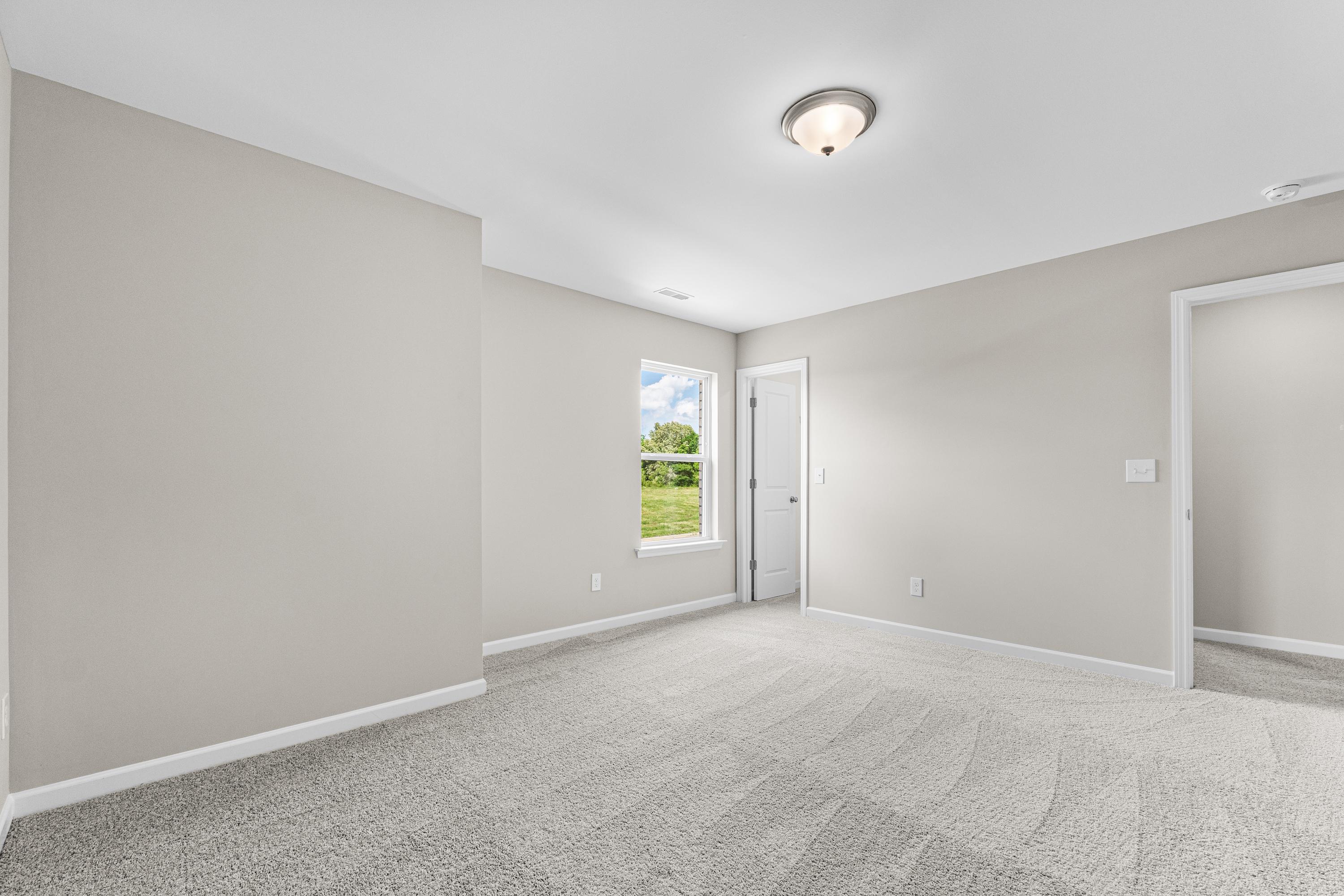 Spacious bedroom interior in The Haven E home design, light gray walls, plush carpet floor, window overlooking greenery