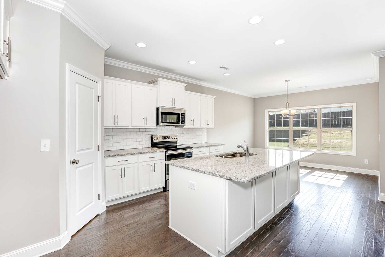 Spacious white kitchen in The Montgomery with large island, subway tile backsplash, stainless appliances, and natural light