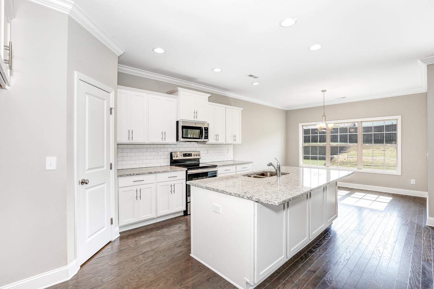 Spacious white kitchen in The Montgomery with large island, subway tile backsplash, stainless appliances, and natural light