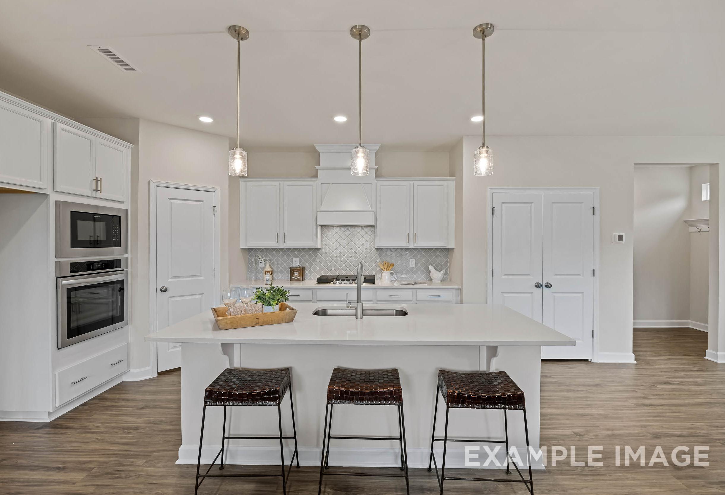 Spacious gourmet kitchen in The Preston A by Davidson Homes featuring white shaker cabinets, large island with bar stools, and pendant lights