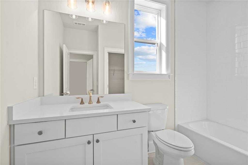 Bright secondary bathroom with white vanity, gold faucet, subway tile tub, and sunny window in Davidson Homes The Arlington A, East Cobb, Georgia