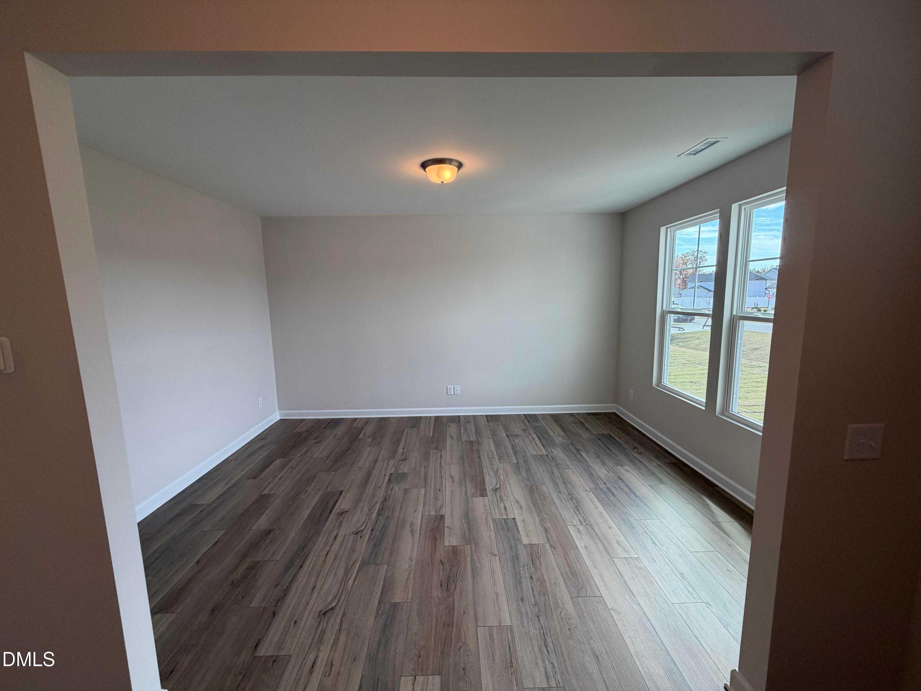 Bright empty living room with beige walls, dark hardwood floors, and large windows in Davidson Homes The Hickory II A, Lillington, NC