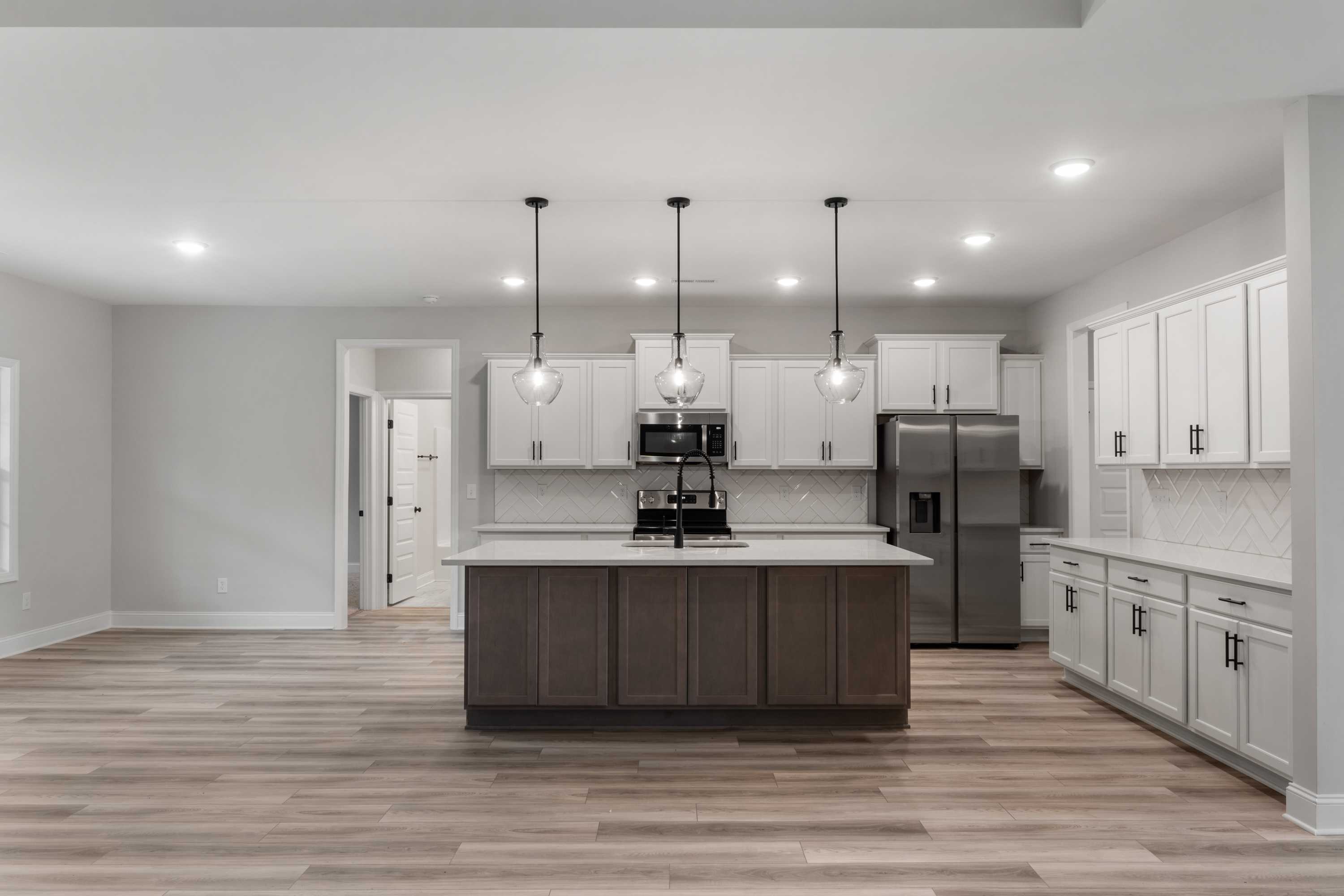 Spacious kitchen in The Oxford Davidson Homes featuring white shaker cabinets, large center island with sink, stainless steel appliances, and hardwood floors