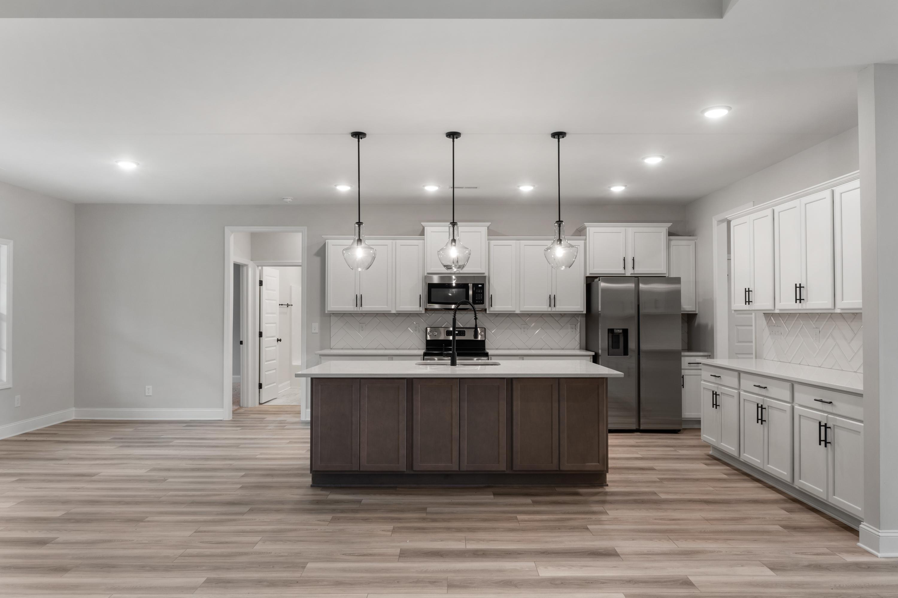 Spacious kitchen in The Oxford Davidson Homes featuring white shaker cabinets, large center island with sink, stainless steel appliances, and hardwood floors