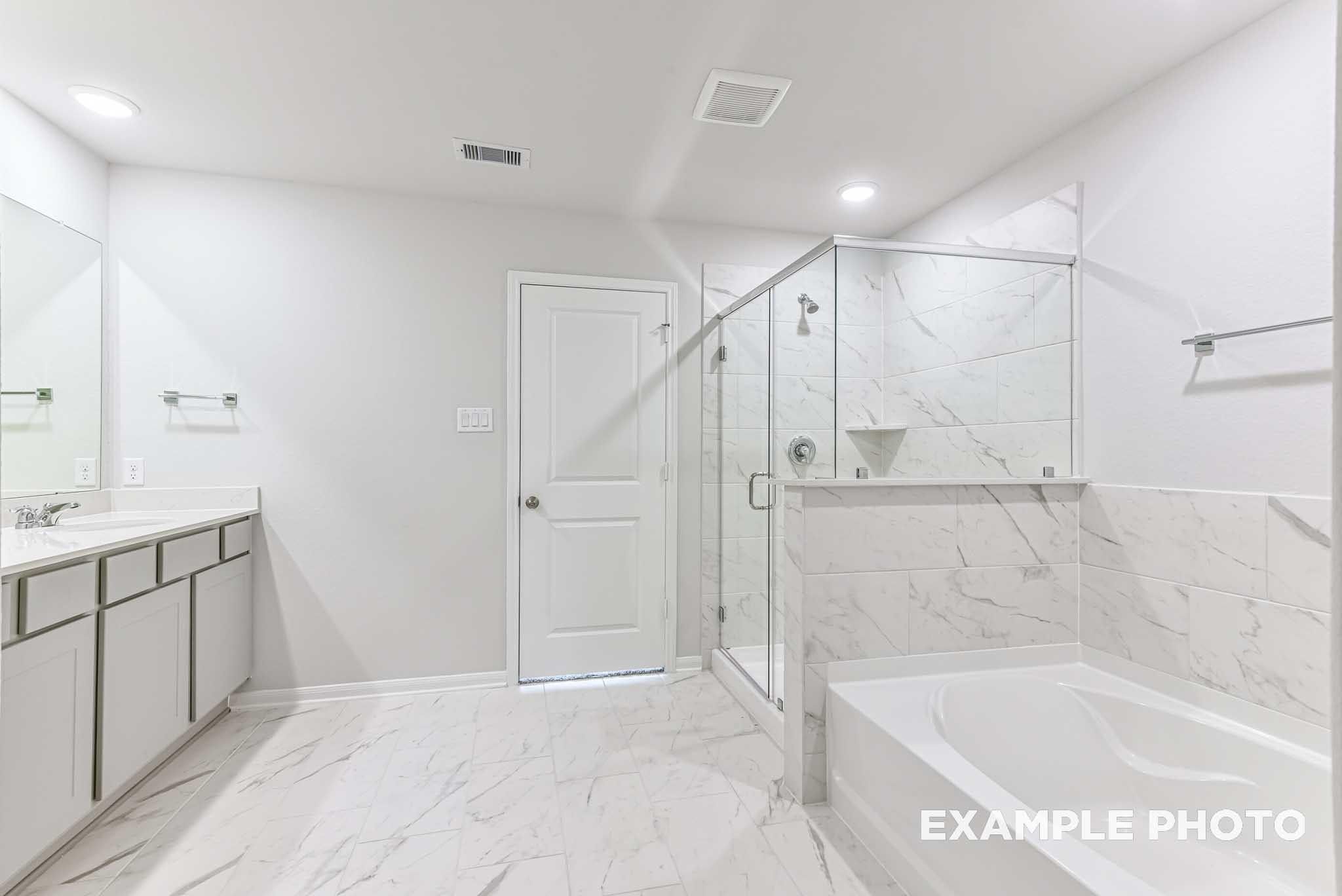 Modern primary bathroom with marble-style tile, glass shower, and deep soaking tub in The Laguna C home, Sunterra, Katy.