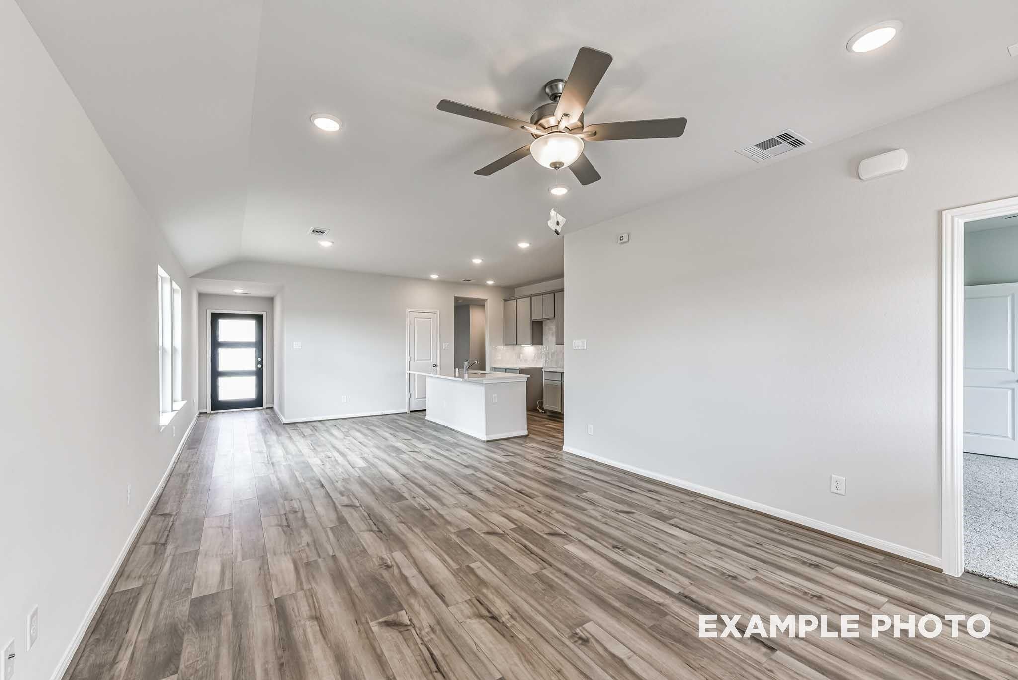 Open-concept living room with vaulted ceiling, ceiling fan, and wood-look flooring in The Costa A floor plan at River Ranch Meadows, Dayton, TX