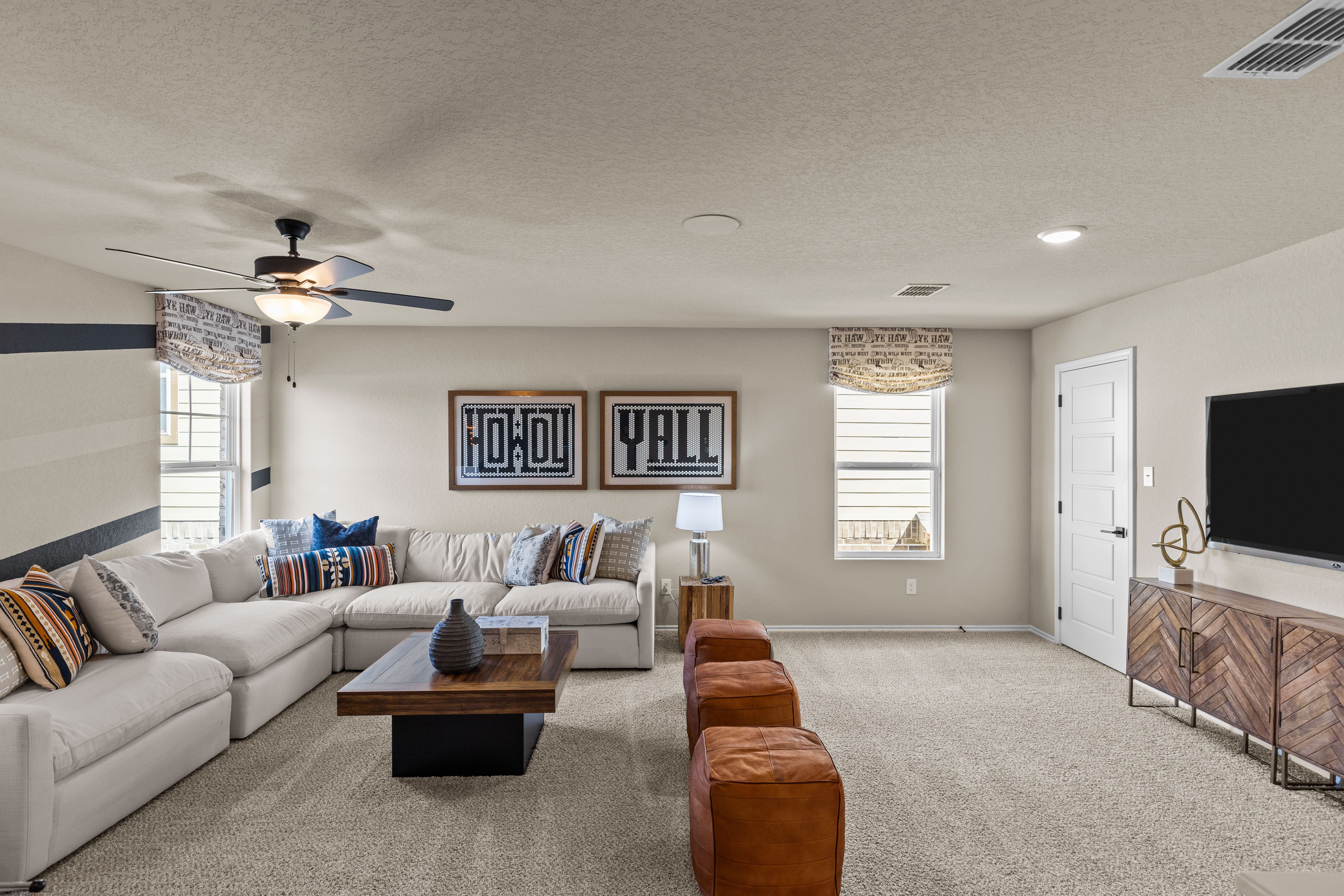 Spacious family room at Morgan Meadows in San Antonio TX featuring L-shaped sectional sofa, ceiling fan, TV, and rustic Howdy Y'all decor