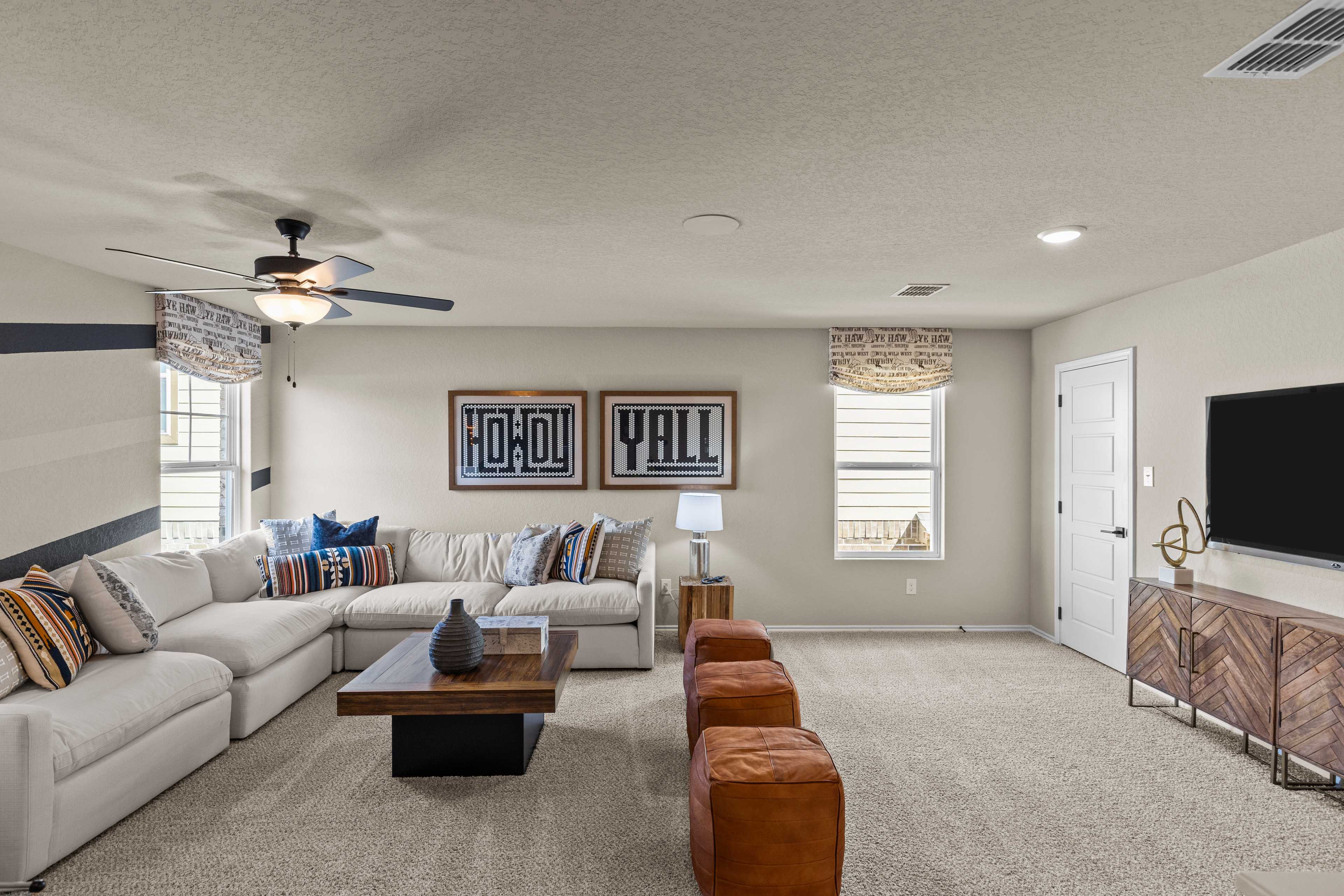 Spacious family room at Morgan Meadows in San Antonio TX featuring L-shaped sectional sofa, ceiling fan, TV, and rustic Howdy Y'all decor