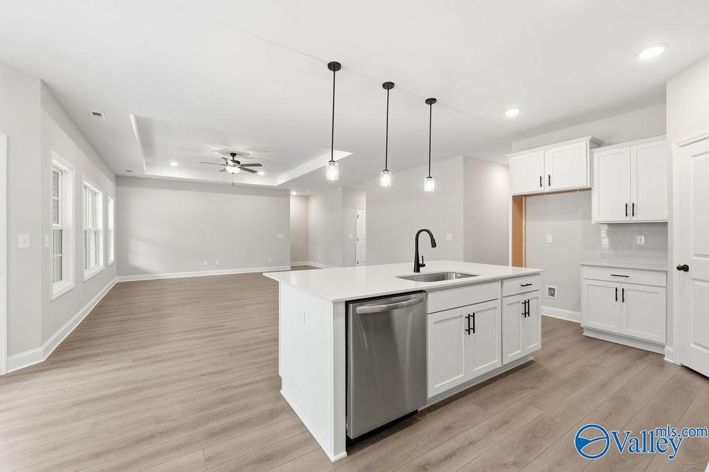 Modern open-concept kitchen with white shaker cabinets, large island sink, stainless dishwasher, and pendant lights in The Rockford B, Hartselle, AL
