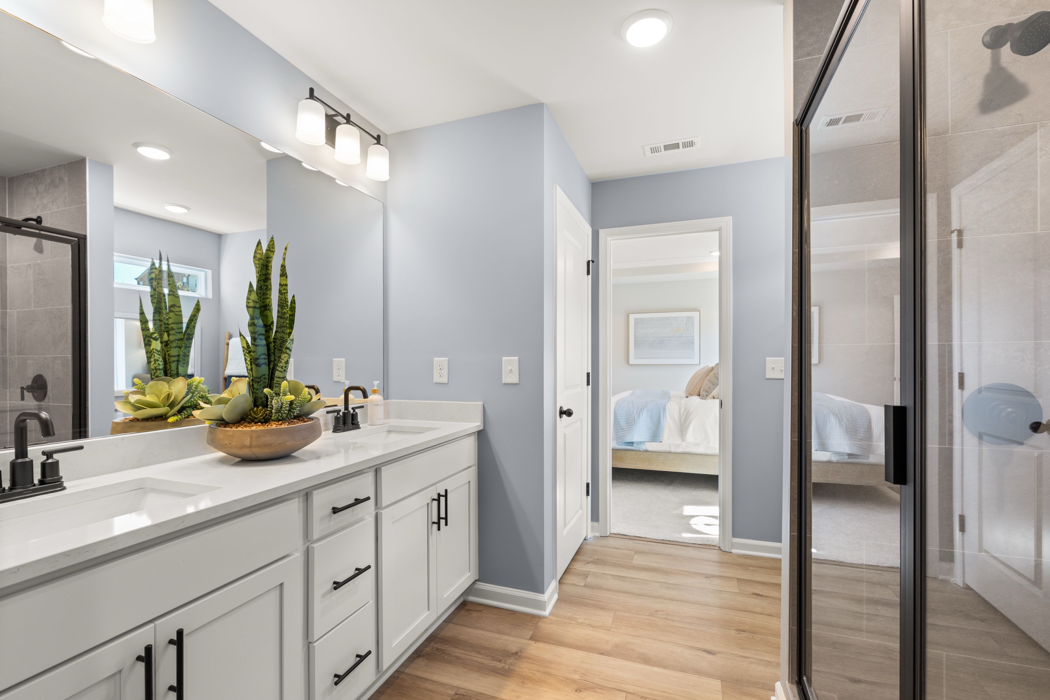 Spacious master bathroom at The Bluffs in Canton GA by Davidson Homes with blue walls, double white vanity, potted plants, and glass shower