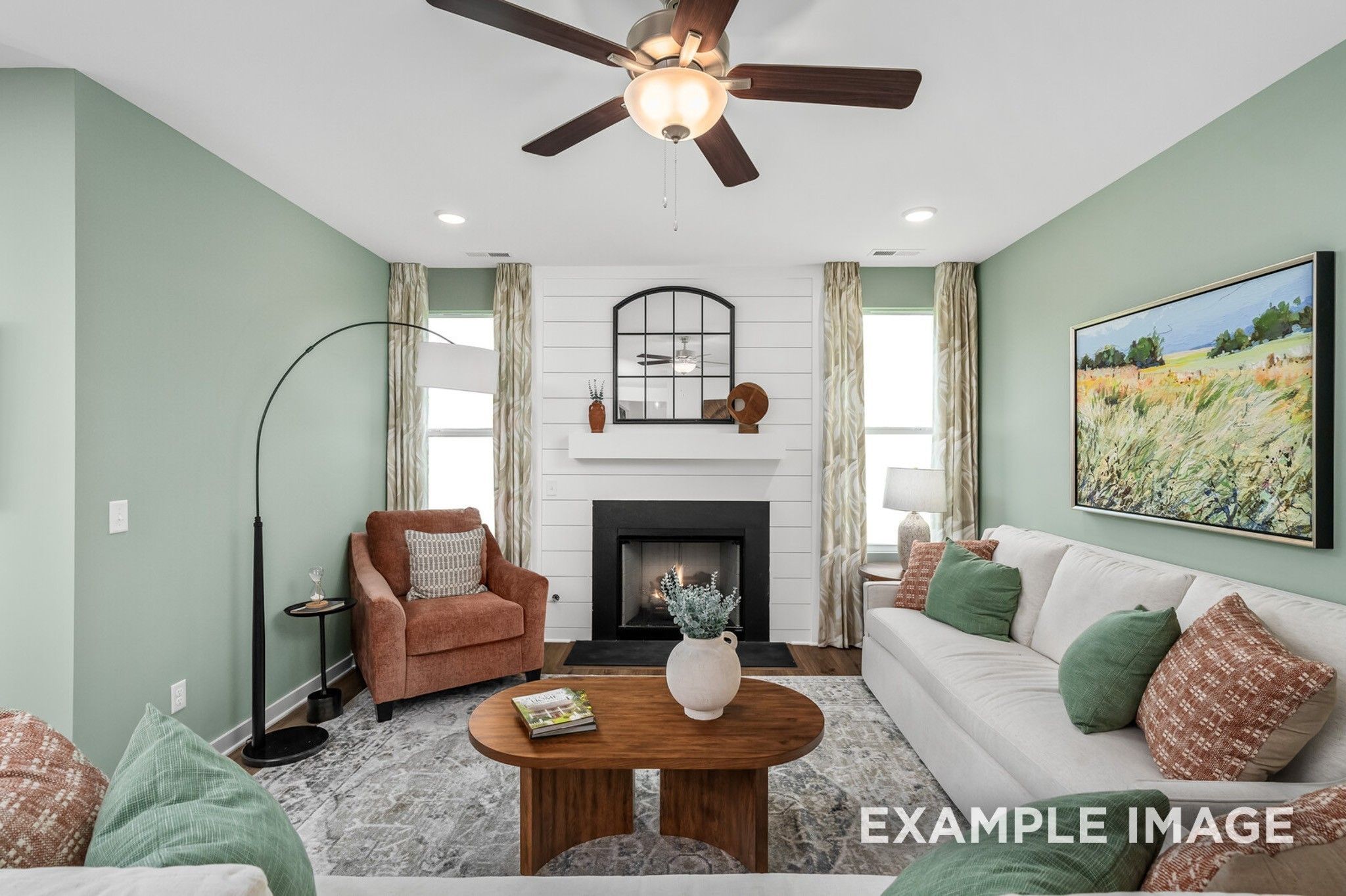 Cozy living room with white sofa, brown armchair, fireplace, and ceiling fan in Davidson Homes The Ash A, Gallatin, Tennessee