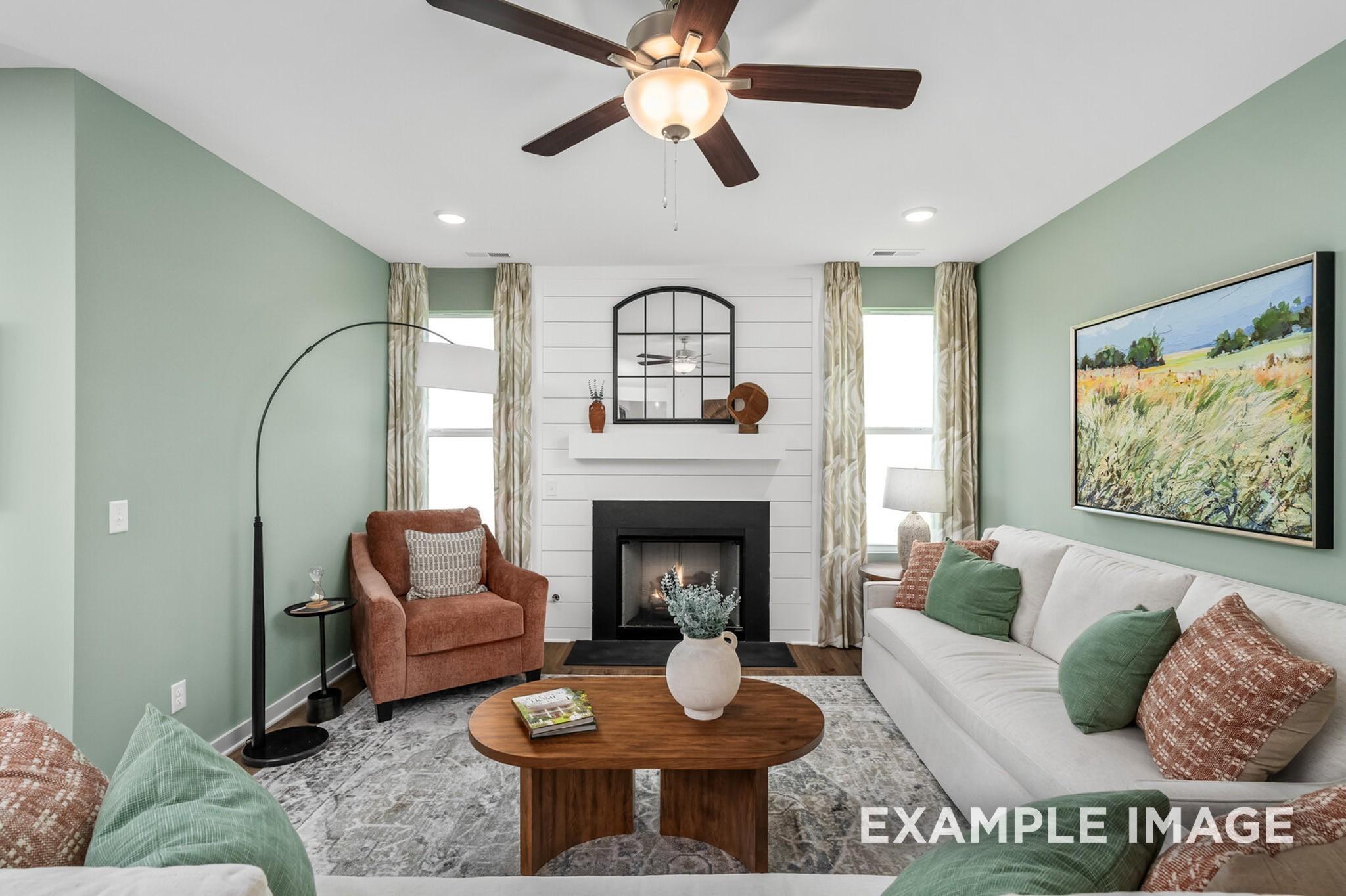 Cozy living room with white sofa, brown armchair, fireplace, and ceiling fan in Davidson Homes The Ash A, Gallatin, Tennessee