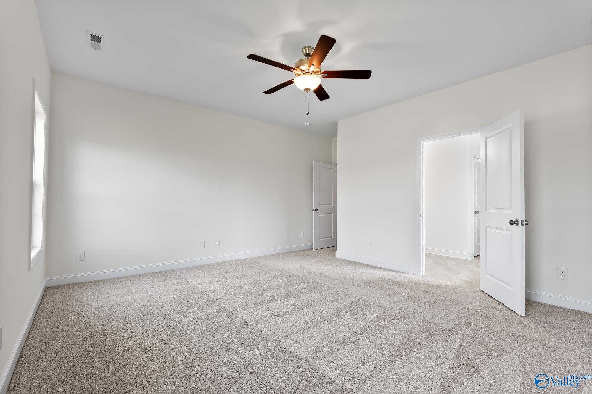 Bright bedroom with ceiling fan, white walls, beige carpet, and open closet door in Davidson Homes The Harrison, Meridianville, Alabama
