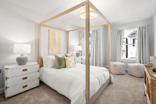 Serene master bedroom in The Washington H townhome with white canopy bed, neutral pillows, lamps, and window drapes