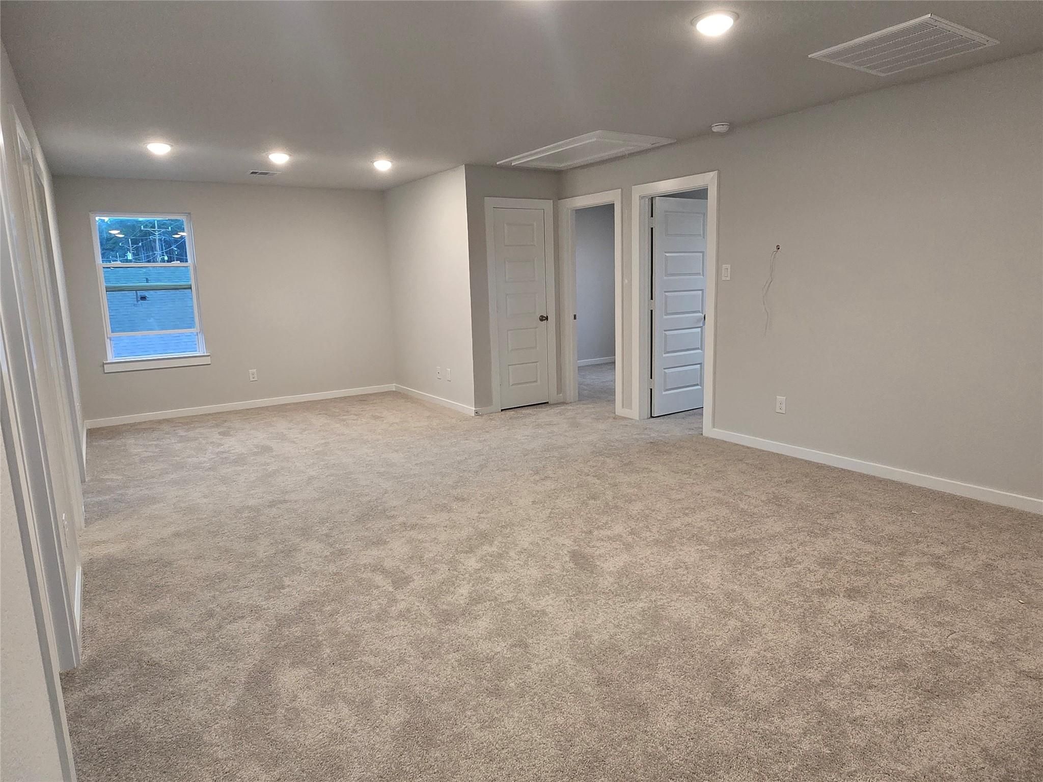 Spacious empty upstairs bedroom with gray walls, beige carpet, recessed lighting, and window view in 5-bedroom The Brazos E home, Cleveland, Texas