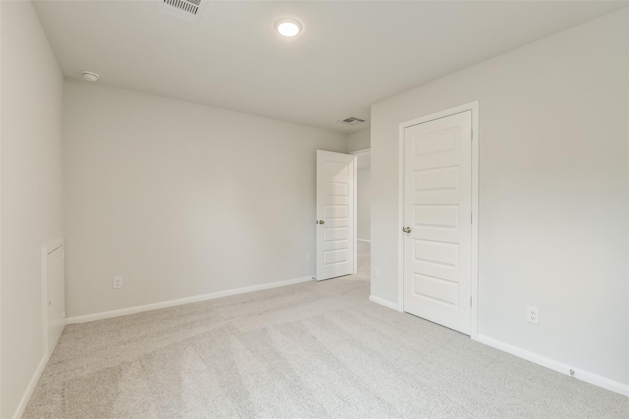Bright secondary bedroom with light gray walls, white paneled doors, and plush carpet in Davidson Homes The Brazos F, Conroe, Texas
