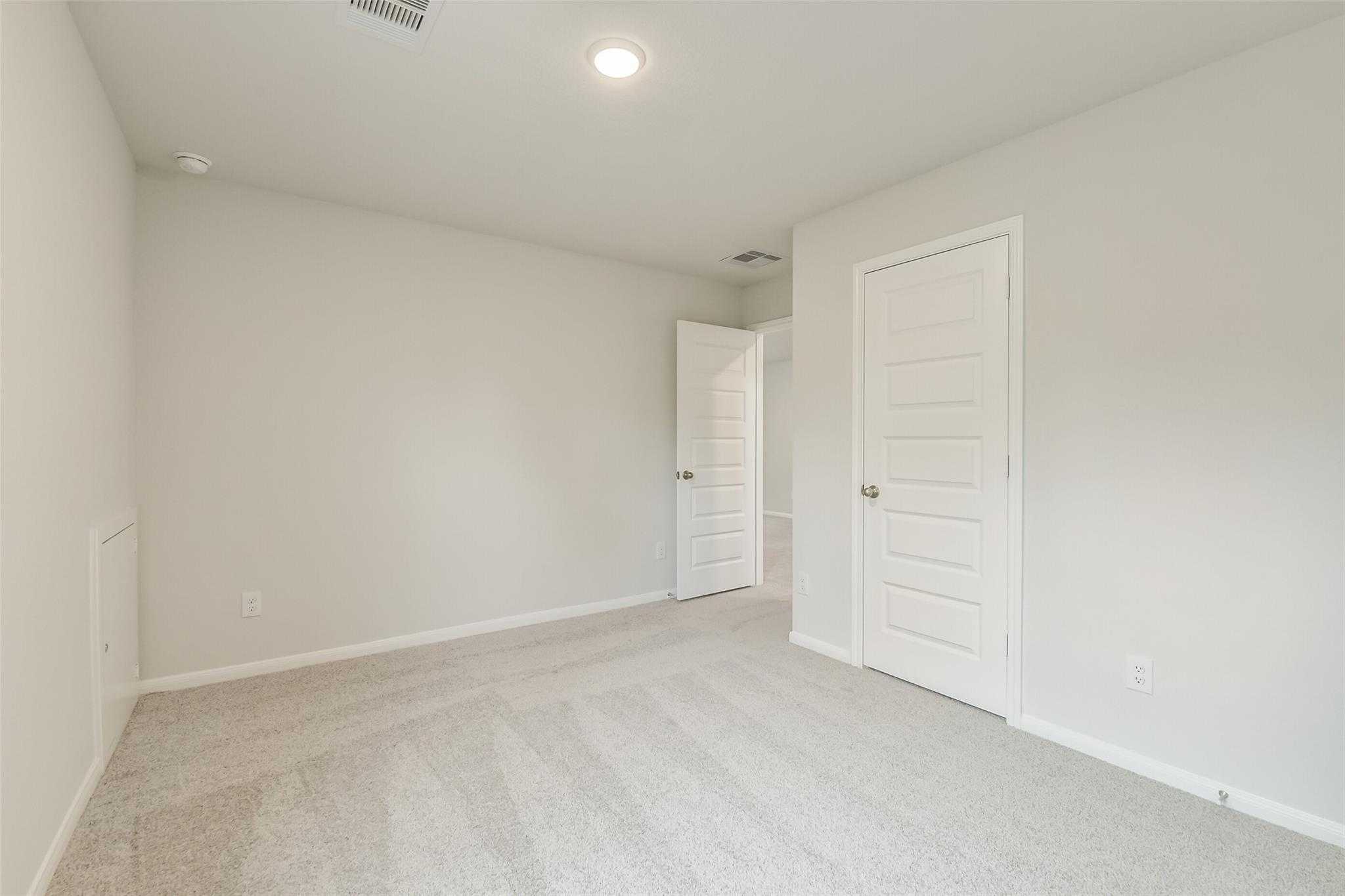 Bright secondary bedroom with light gray walls, white paneled doors, and plush carpet in Davidson Homes The Brazos F, Conroe, Texas