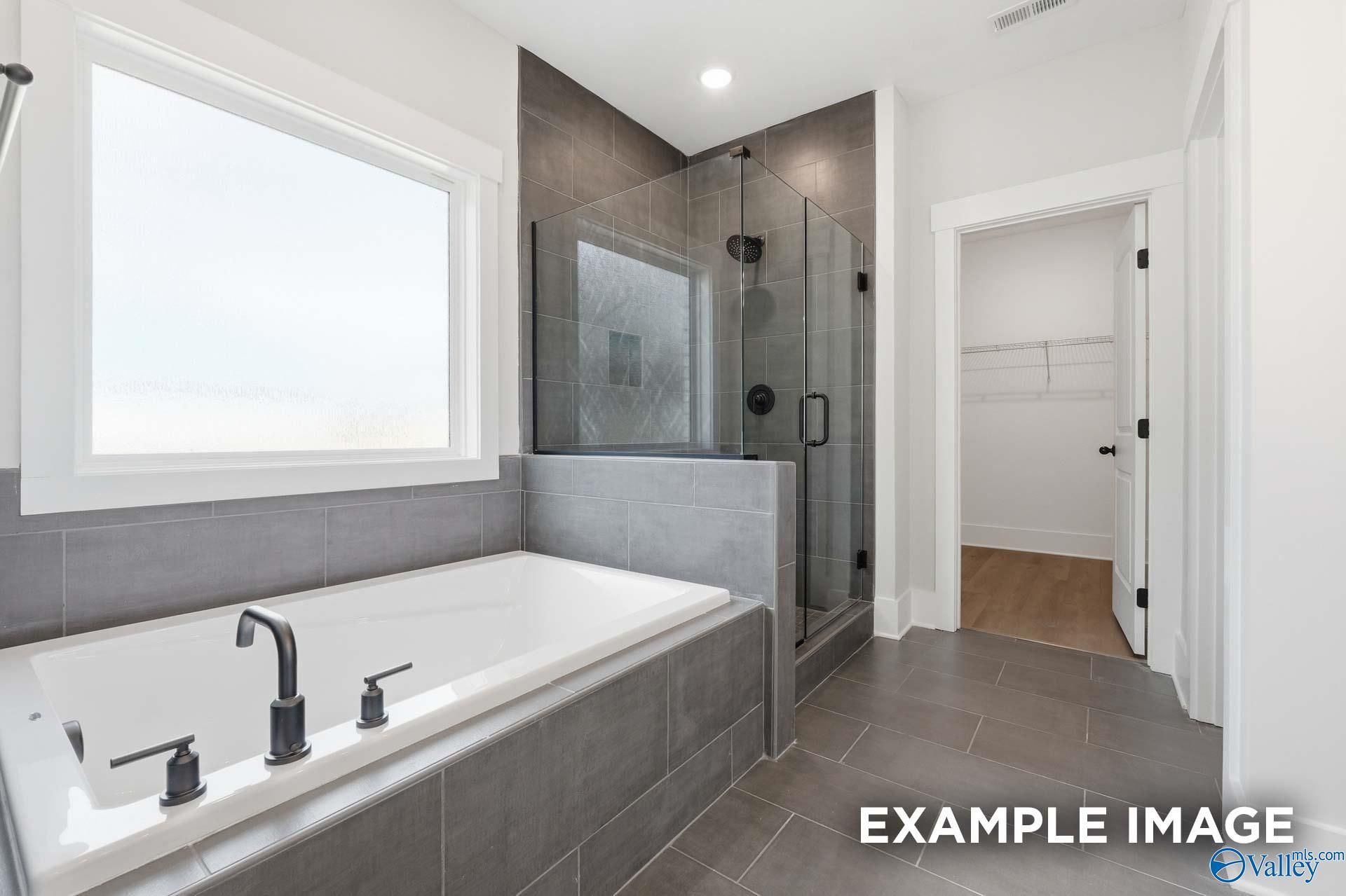 Modern primary bathroom with soaking tub, glass-enclosed shower, and walk-in closet in The Rockford by Davidson Homes.