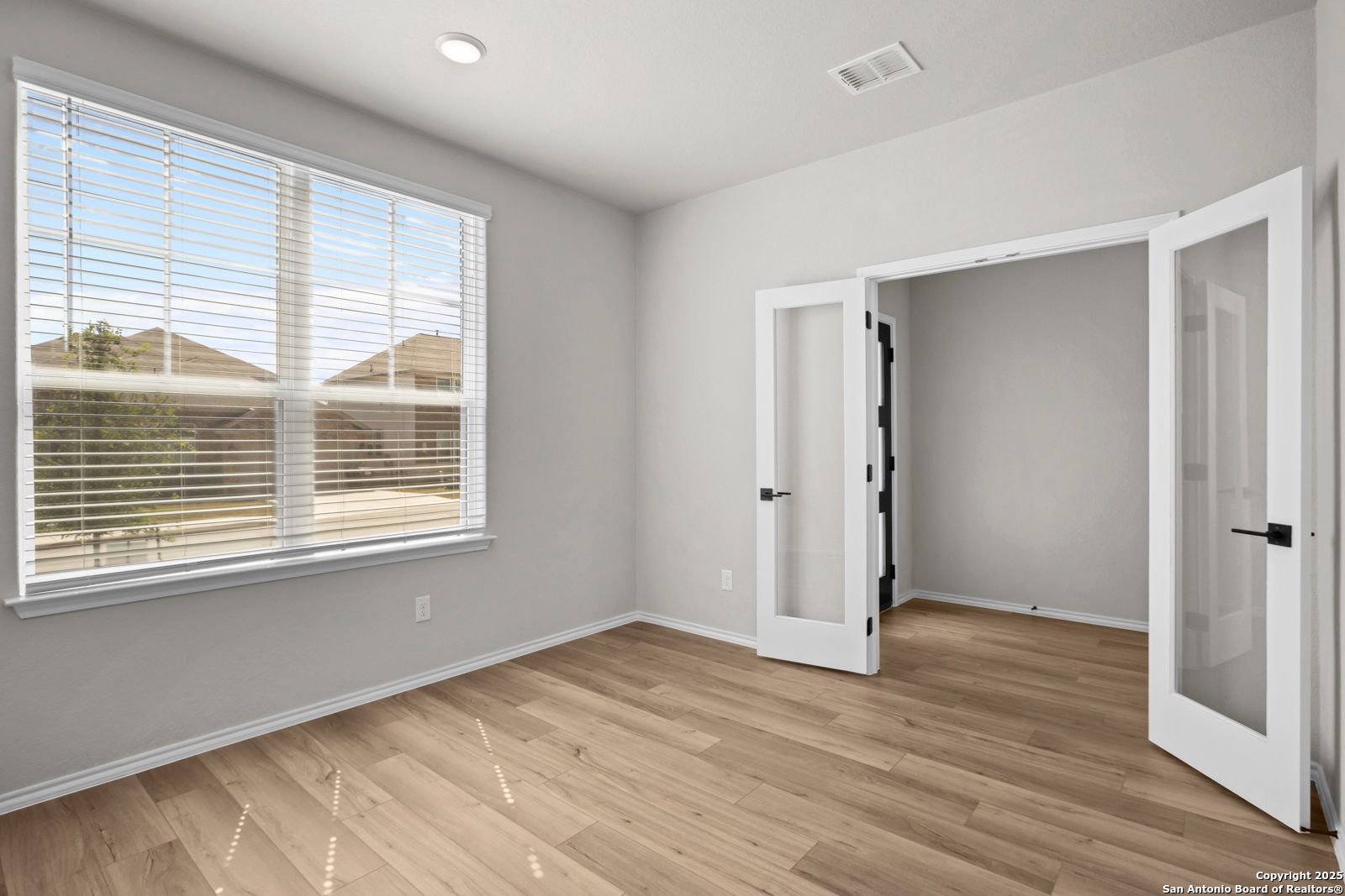 Bright empty room with hardwood floors, open French doors, and large window in Davidson Homes Sequoia A, Converse, Texas