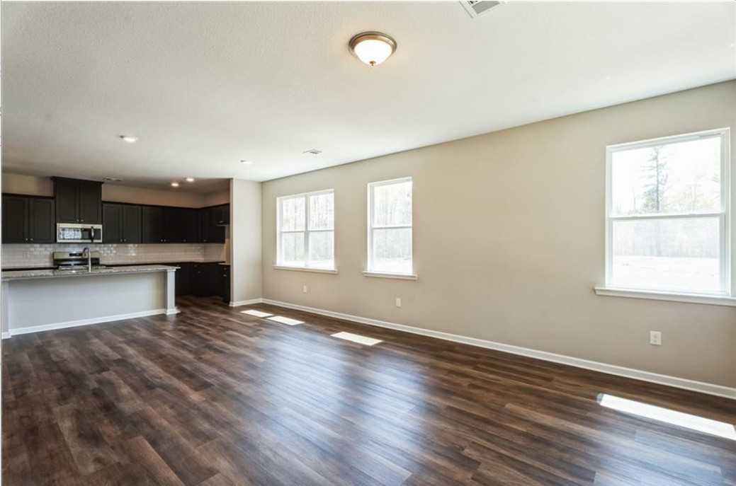 Open-concept kitchen and living space with dark cabinets, white island, wood-look floors, and large windows in The Aurora A, Cusseta, Alabama