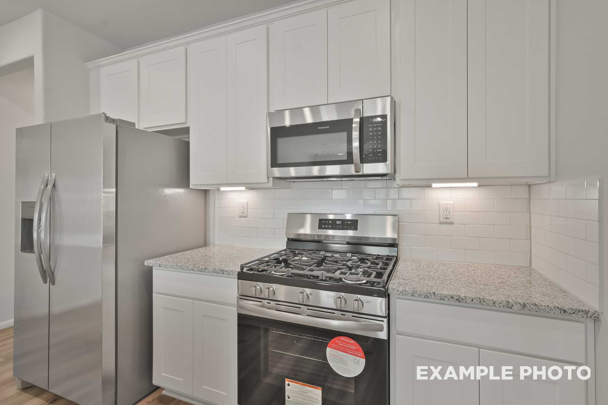 Modern kitchen in The Comal plan featuring white shaker cabinets, stainless steel appliances, gas cooktop, and granite counters