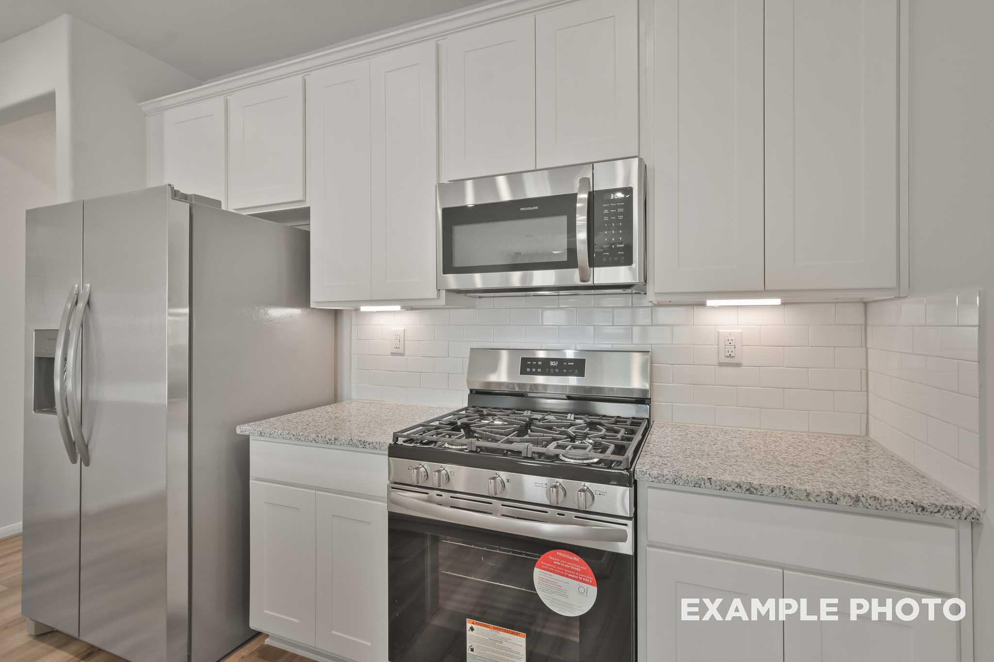 Modern kitchen in The Comal plan featuring white shaker cabinets, stainless steel appliances, gas cooktop, and granite counters