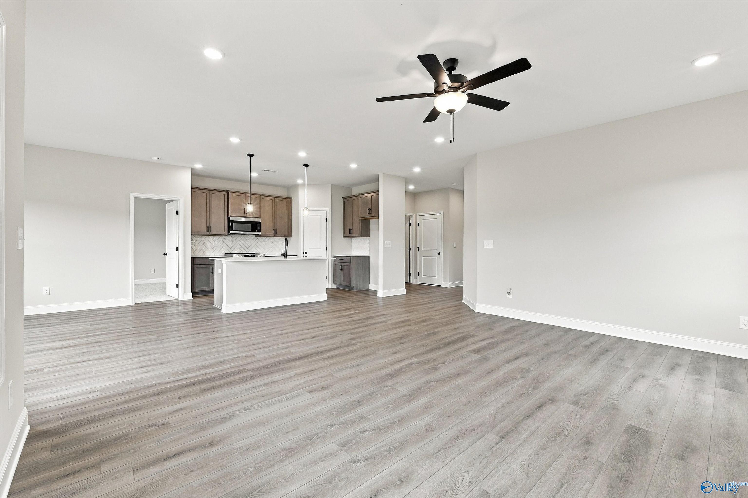 Open-concept living room and kitchen with gray plank flooring, island, and ceiling fan in The Franklin C plan, Athens, Alabama