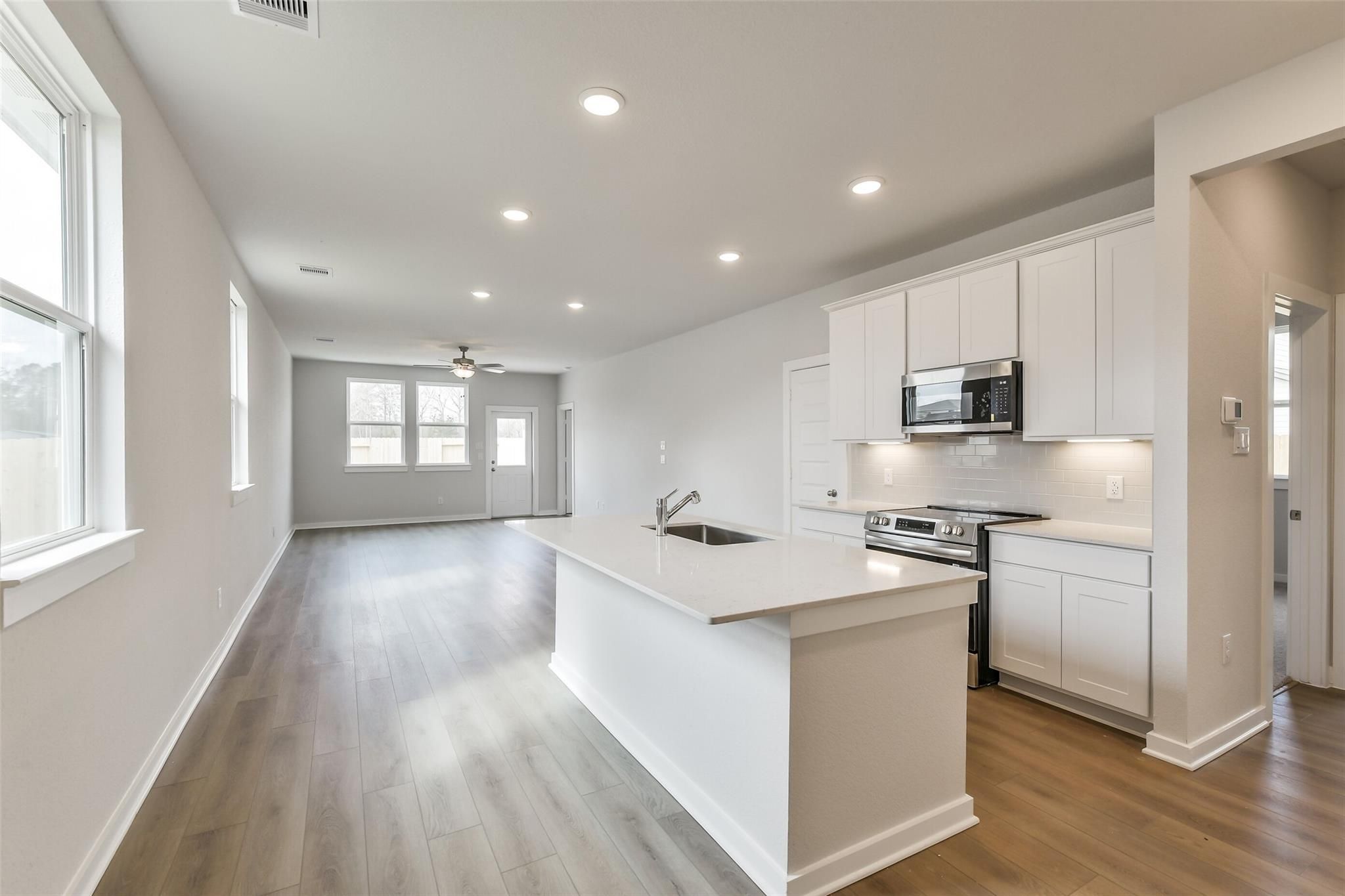 Open-concept kitchen with white island, stainless appliances, and laminate floors in Davidson Homes The Frio G, Cleveland Texas
