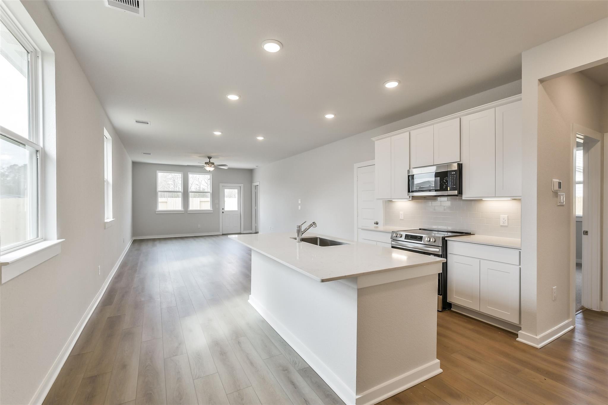 Open-concept kitchen with white island, stainless appliances, and laminate floors in Davidson Homes The Frio G, Cleveland Texas