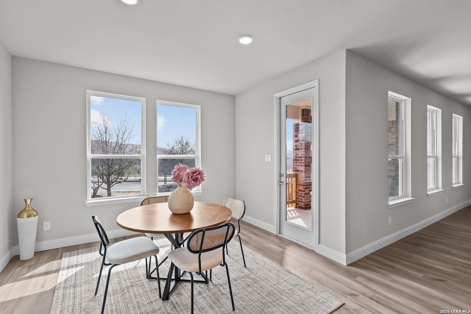 Elegant dining area with round wooden table, pink floral vase, large windows, and sliding door to covered patio in Davidson Homes Rockford G, Ladera San Antonio