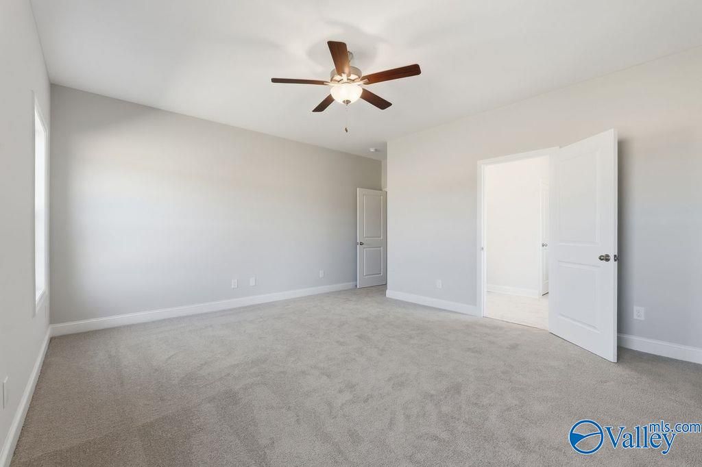 Spacious bedroom with ceiling fan, gray carpet, neutral walls, and open doorway in Davidson Homes The Harrison, Hartselle, Alabama