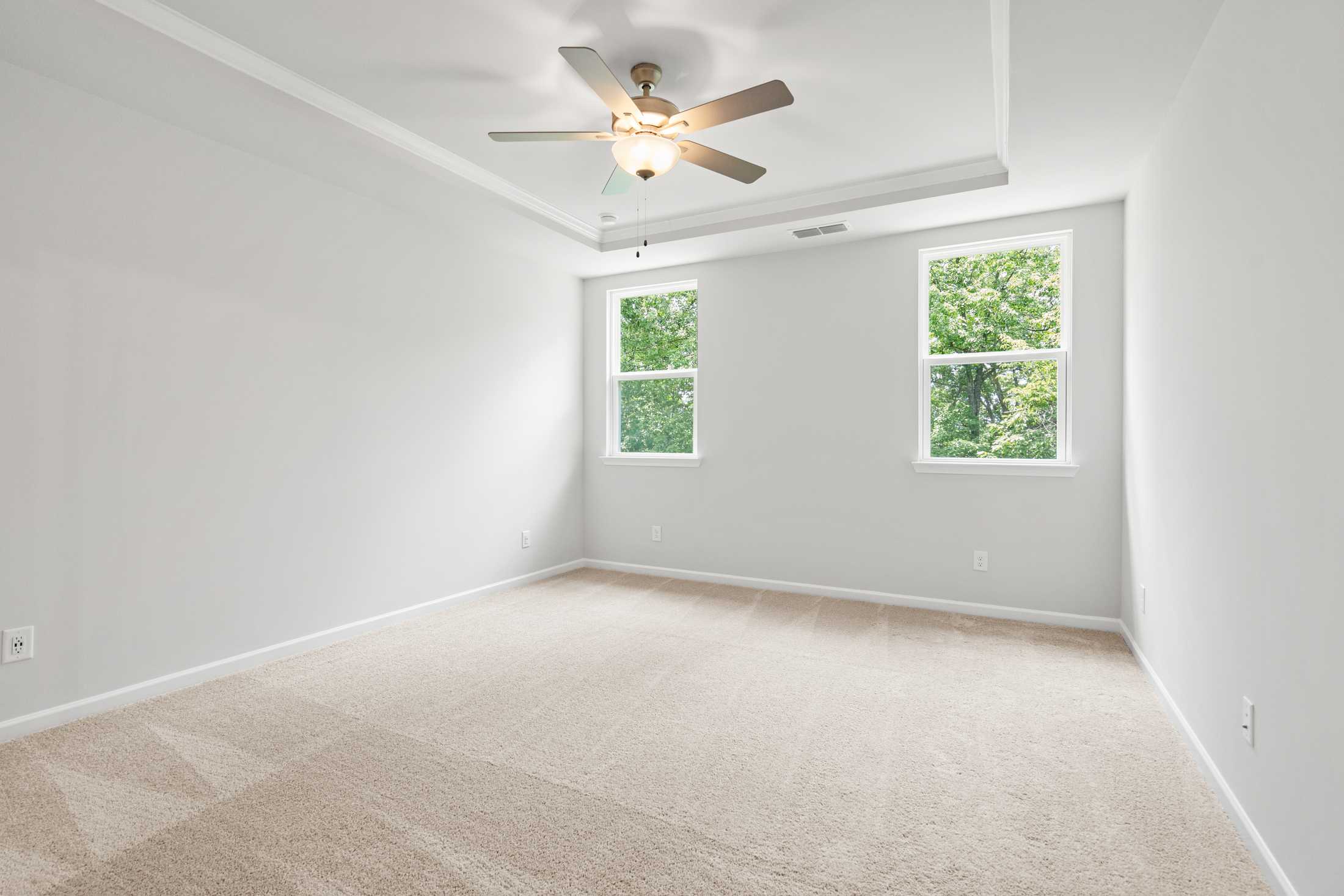 Spacious empty bedroom in The Ash B home at Wehunt Meadows with beige carpet, ceiling fan, tray ceiling, and large windows overlooking greenery