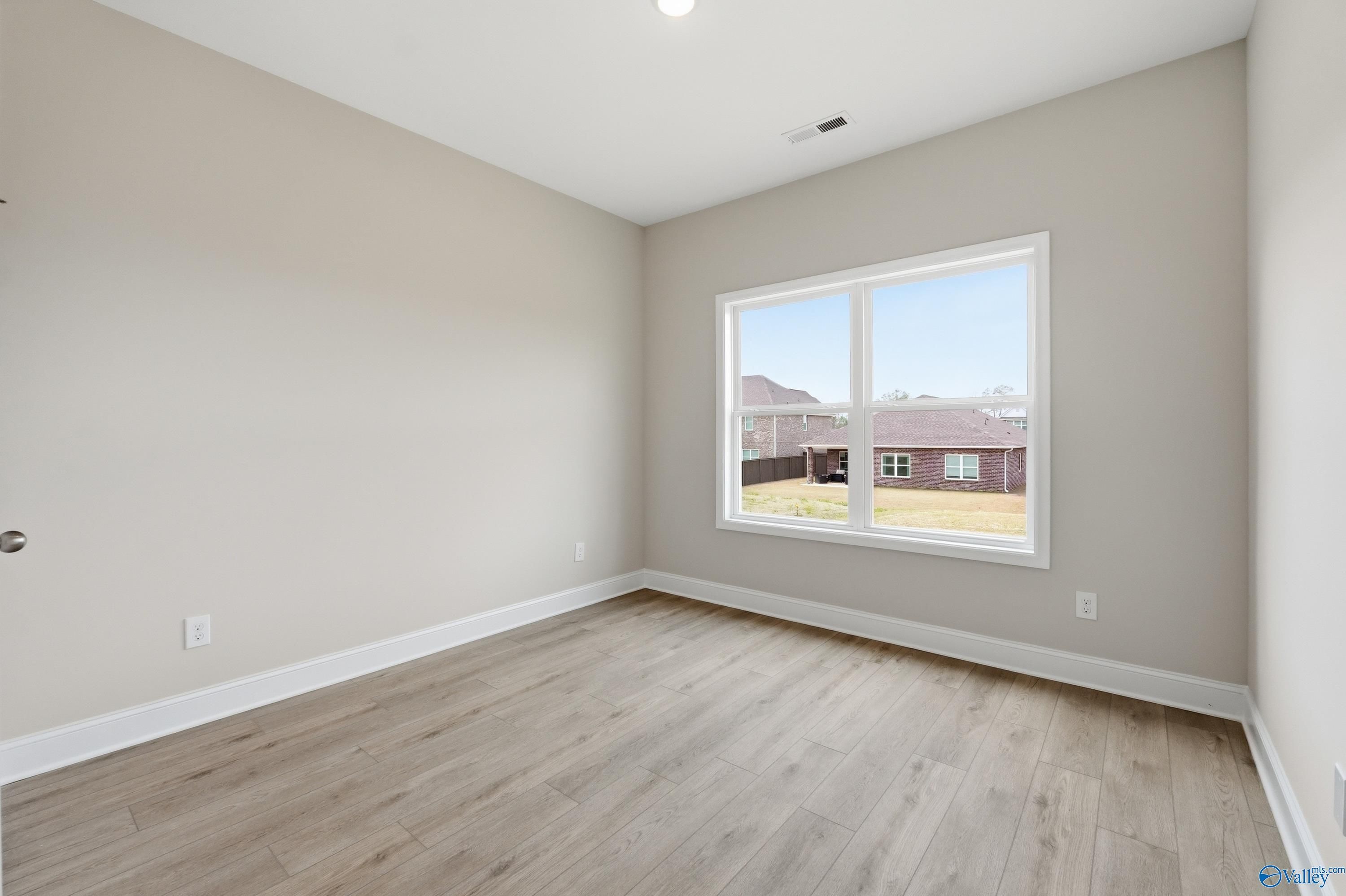 Bright bedroom with beige walls, large window overlooking yard, and hardwood floors in Davidson Homes Shelby B, New Market, Alabama