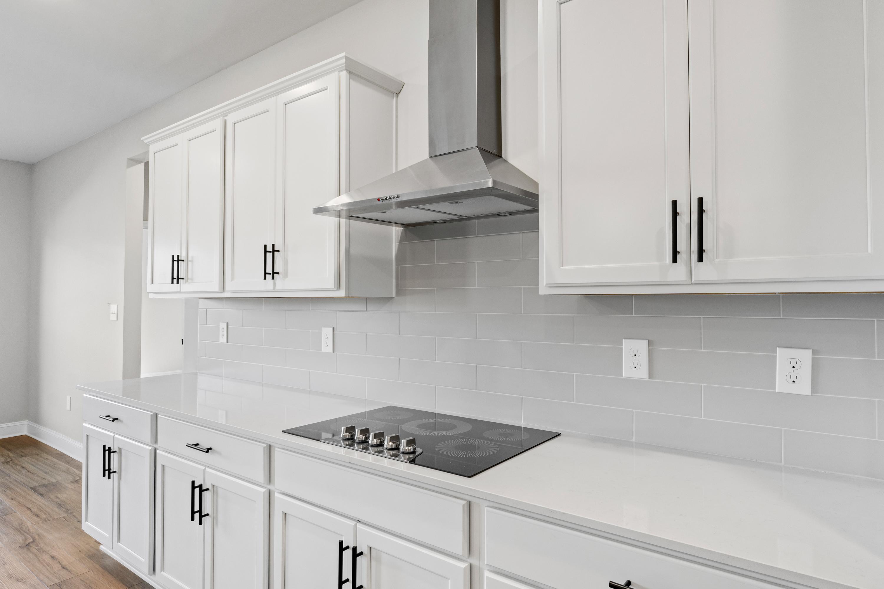 Spacious white shaker kitchen in The Valencia with stainless steel cooktop, hood, subway tile backsplash, quartz counters